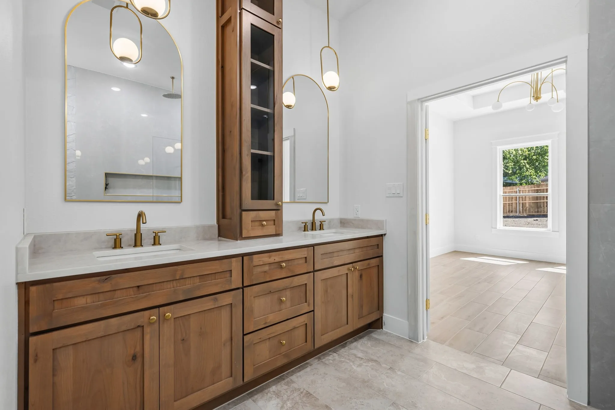 Dual vanity with wood cabinetry, light-toned countertop, and gold-finish fixtures