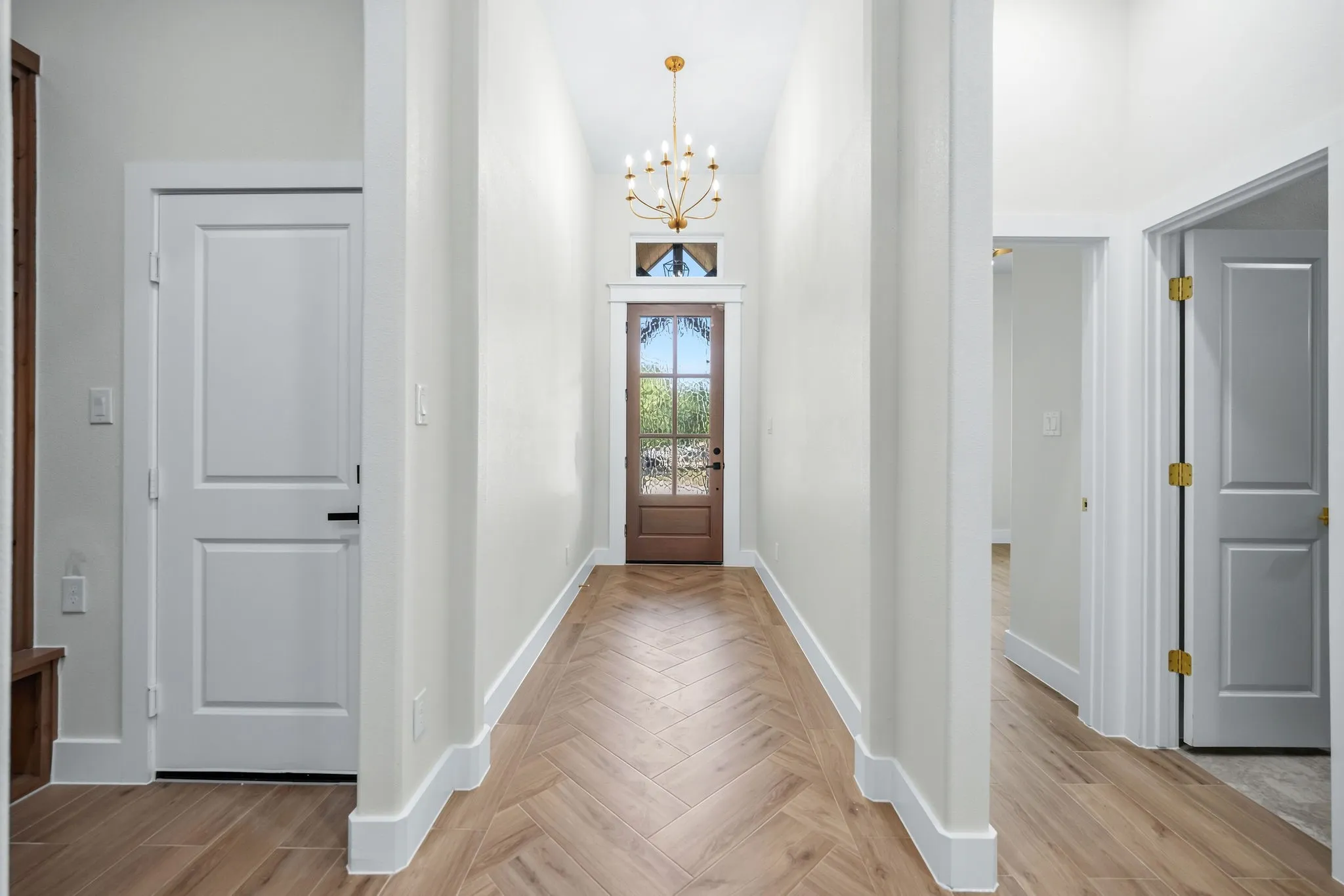 Herringbone wood-finish flooring, recessed lighting, and a chandelier illuminate a spacious hallway