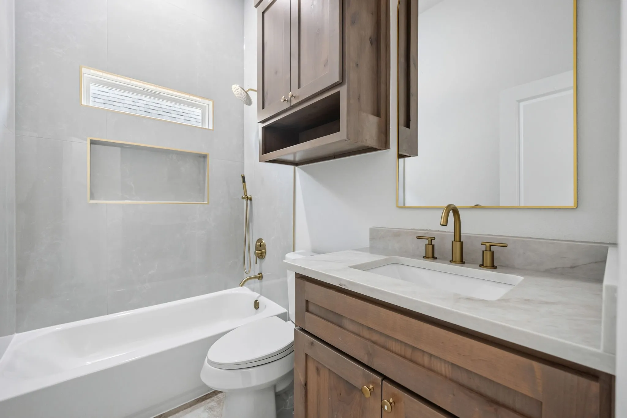 White porcelain bathtub with integrated shower, brass fixtures, and a recessed shower niche