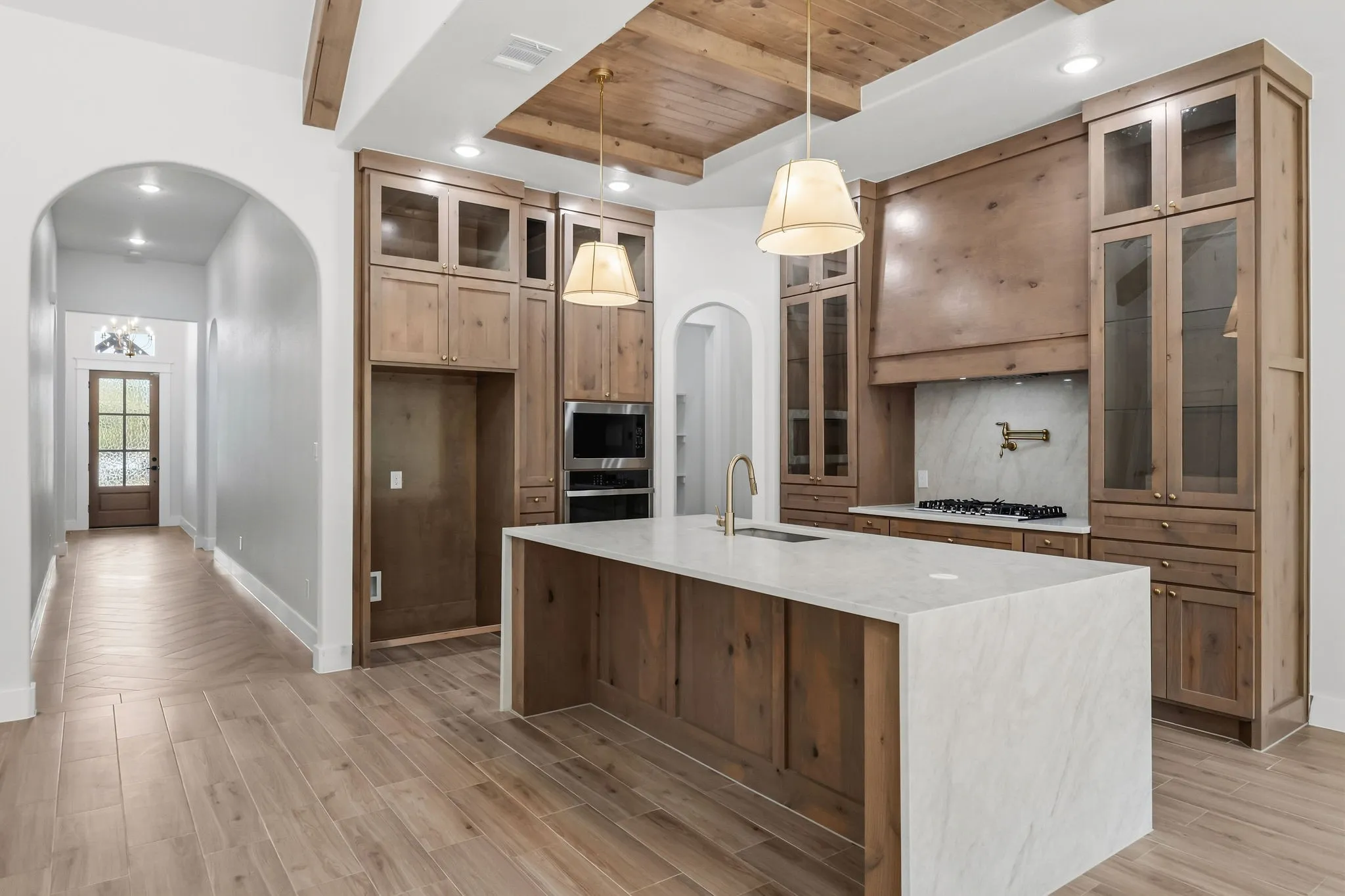 Kitchen featuring a large island with a waterfall countertop, integrated cooktop, wood cabinetry, and a wood-paneled ceiling