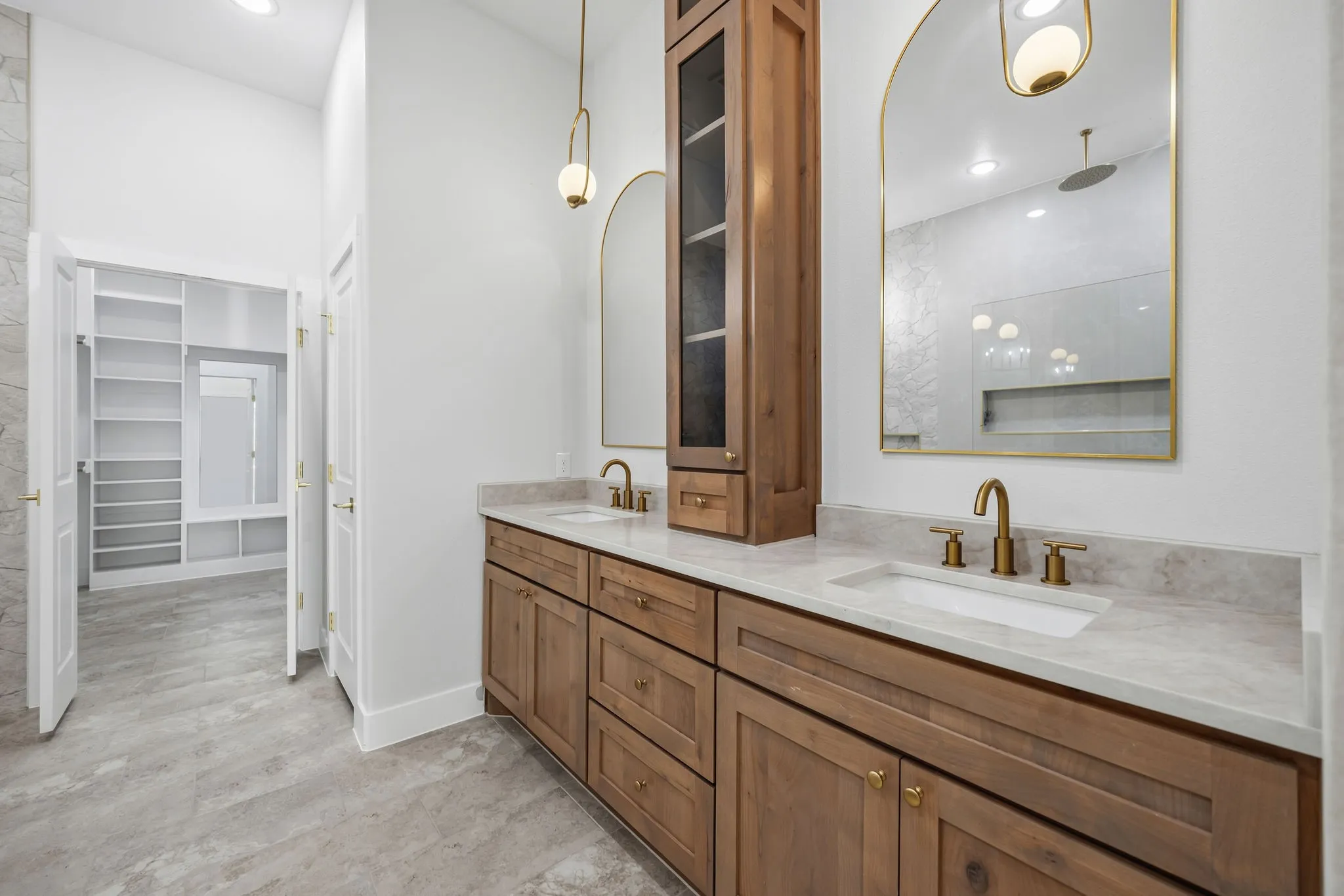Dual wood-finish vanity with integrated sinks and brass fixtures, accompanied by a tall wood-finish storage cabinet