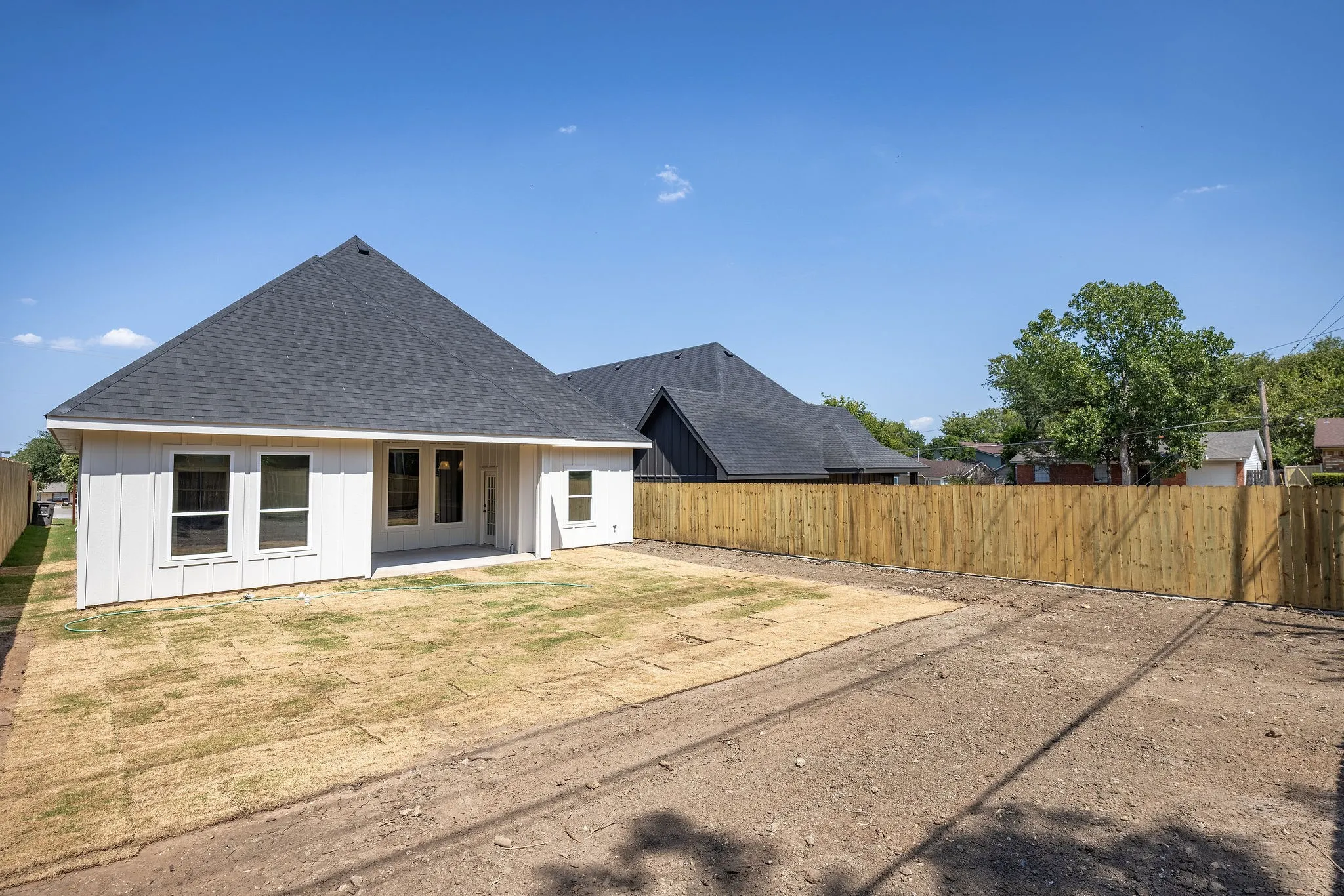 Rear exterior featuring white vertical siding, a dark shingle roof, multiple windows, a covered patio, and a newly installed wood fence