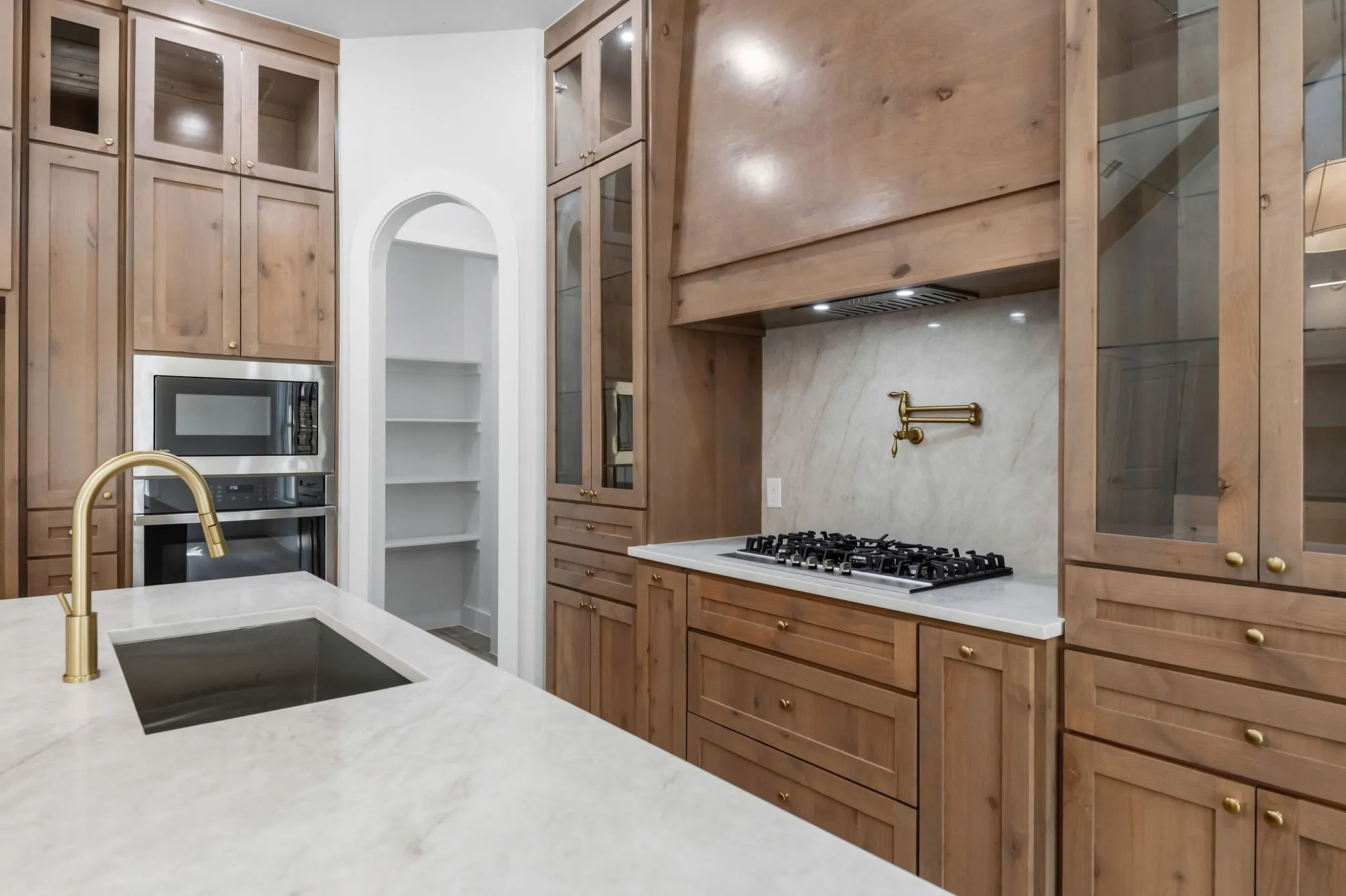 Kitchen featuring wood cabinetry, integrated stainless steel appliances, a gas cooktop with pot filler, and a large central island with an undermount sink