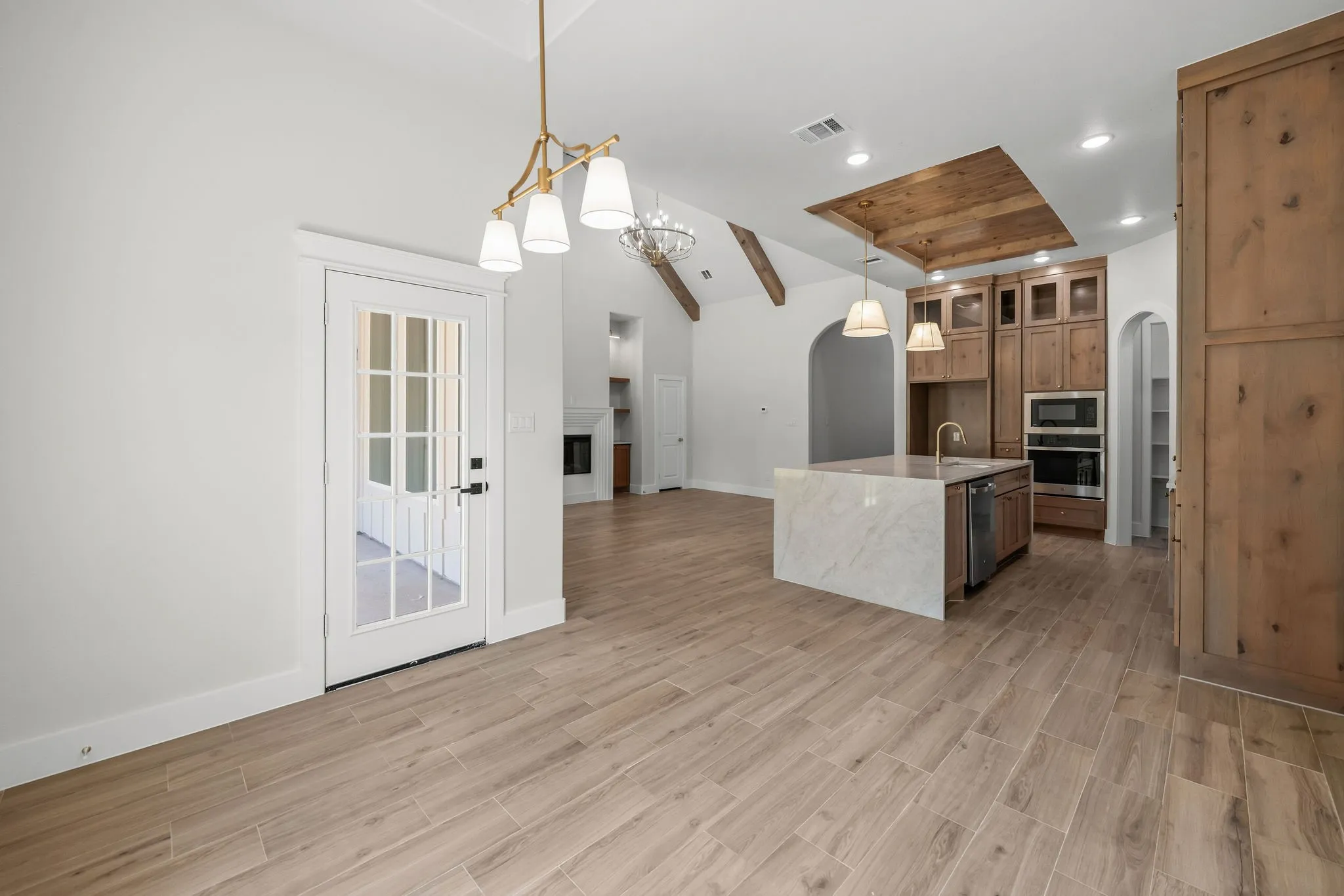 Vaulted ceiling with exposed beams, wood-finish flooring, kitchen island with integrated sink, recessed ceiling lighting, and built-in kitchen appliances
