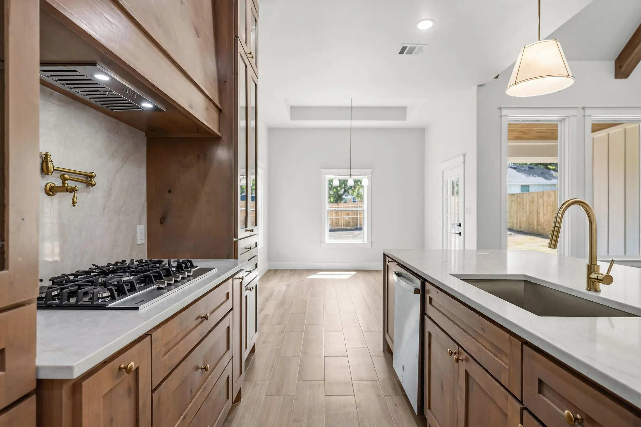 Kitchen featuring wood-finish cabinetry, white countertops, built-in gas range, stainless steel dishwasher, and a single-basin sink with a gold-finish faucet