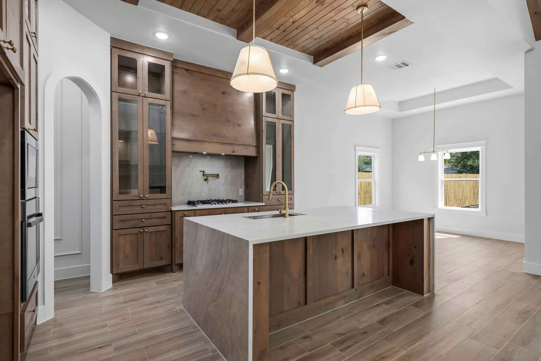 Kitchen featuring wood-finish flooring, a large island with a light-toned countertop, wood-finish cabinetry, a built-in oven, and a wood-paneled ceiling with recessed lighting