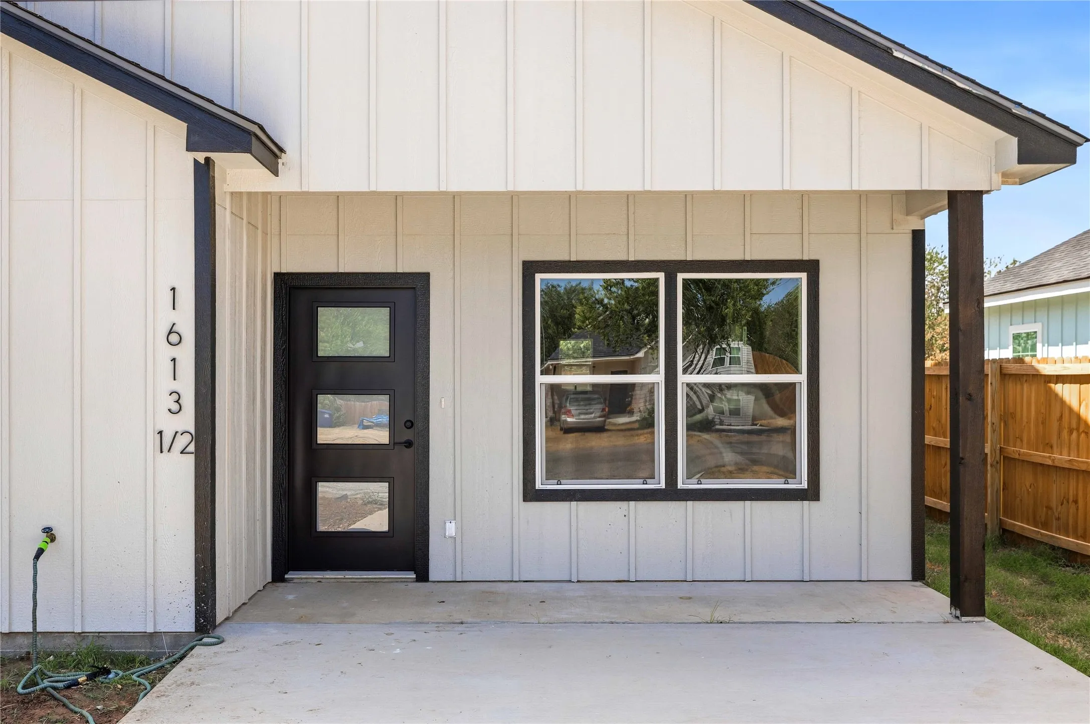 Board and batten siding, dark trim accents, covered porch, contemporary entry door  and large windows