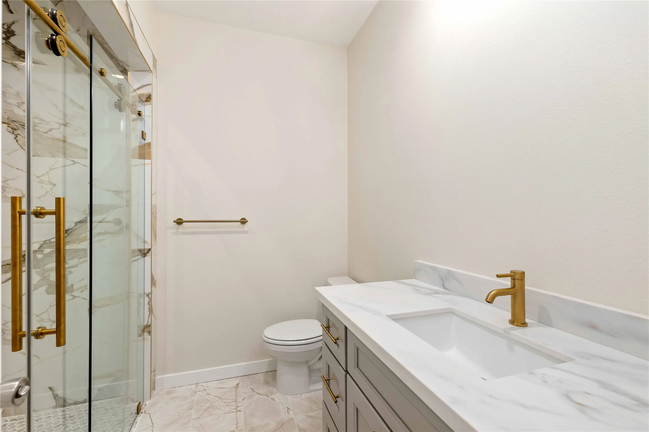 Walk-in shower with clear glass enclosure, gold-toned hardware, and marble-finish tile. Mirrors will be installed