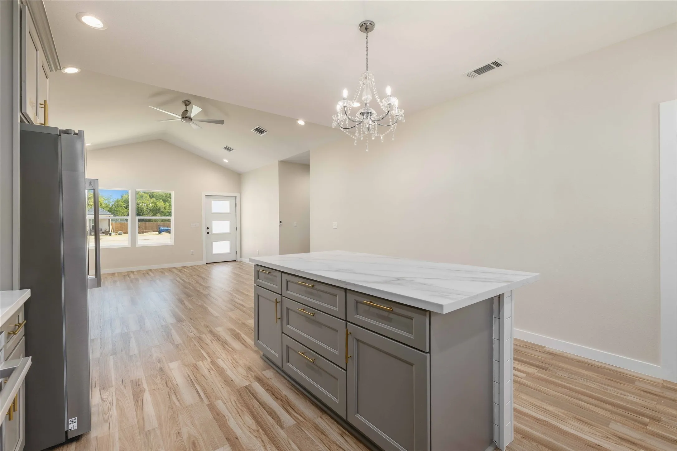 Central island with a quartz countertop, wood-finish flooring, vaulted ceiling, recessed lighting, and a contemporary chandelier