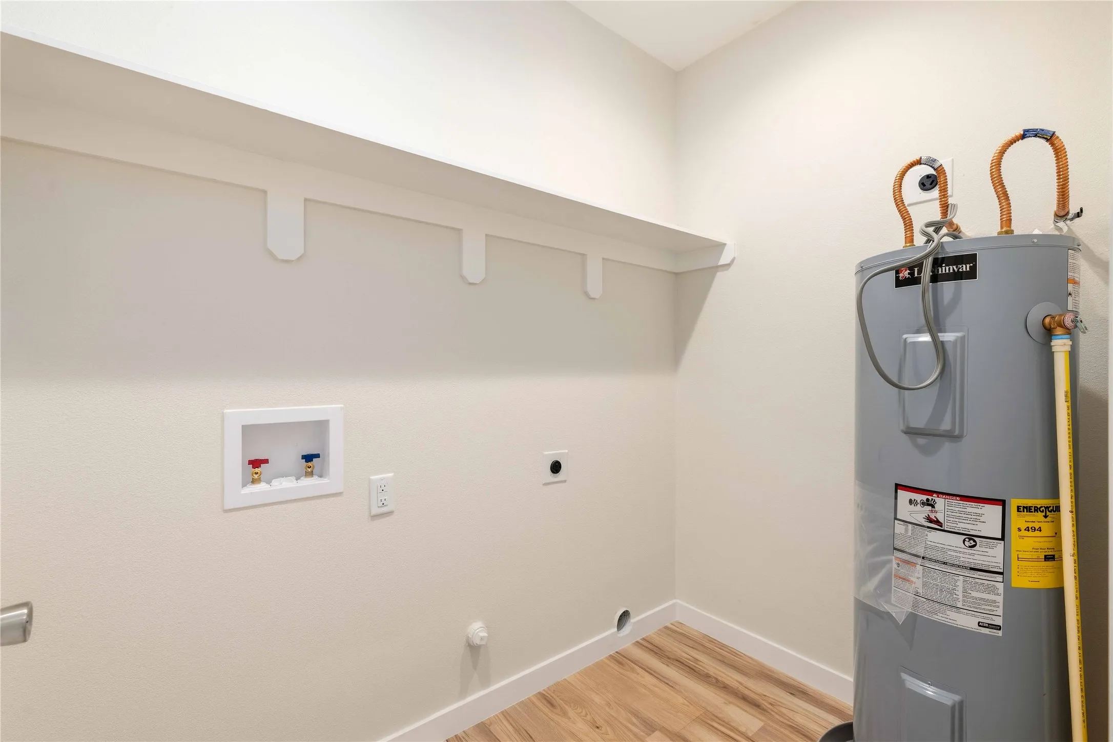 Utility area with wood-finish flooring, a wall-mounted shelf, and a water heater
