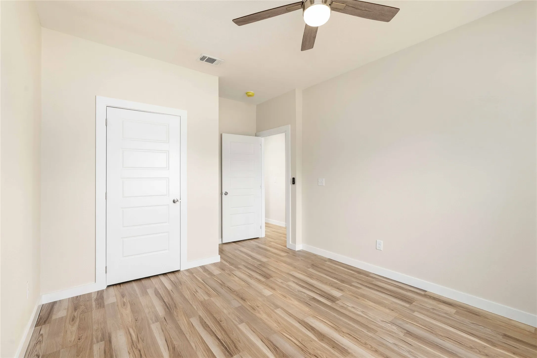 Wood-finish flooring, ceiling fan with integrated lighting, white paneled doors, and light-toned walls