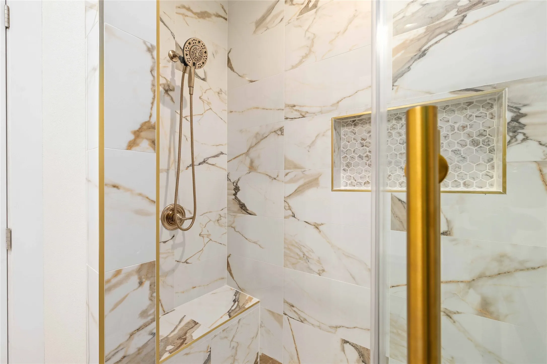 Shower featuring large format marble-look tile,  a built-in bench