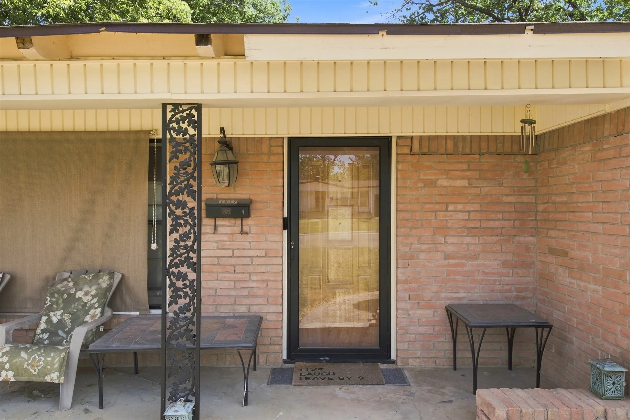 Brick exterior featuring a covered porch, decorative metal column, porch light, and glass panel entry door