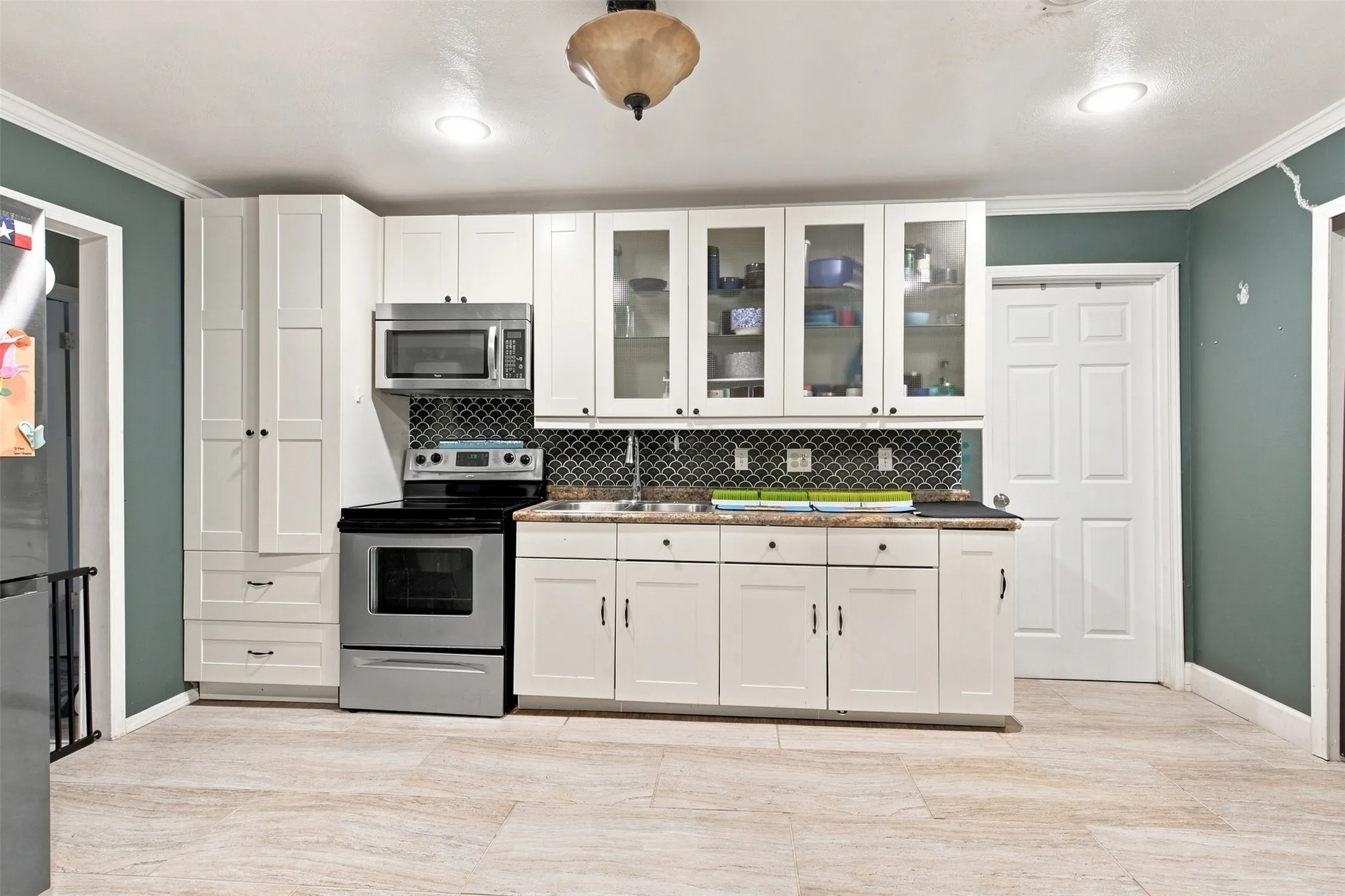 White shaker-style cabinetry with glass-front uppers, stainless steel appliances, dark mosaic tile backsplash, and light-toned flooring