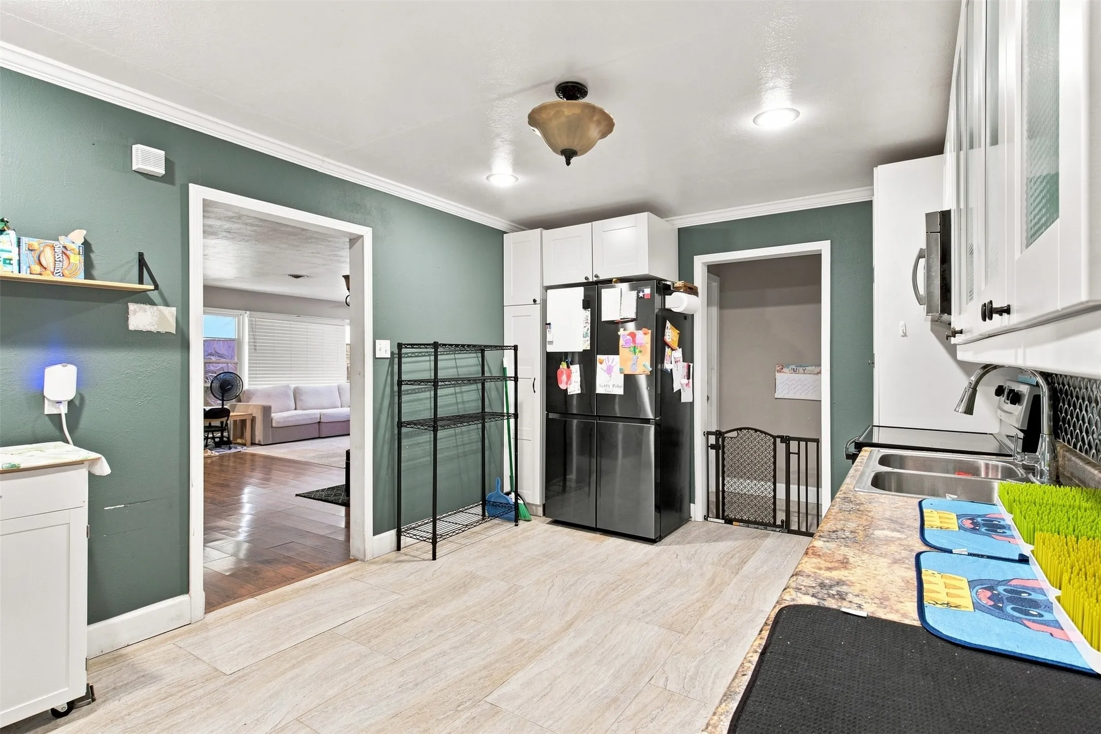 Kitchen featuring light-toned flooring, white upper cabinetry, and a dark tile backsplash