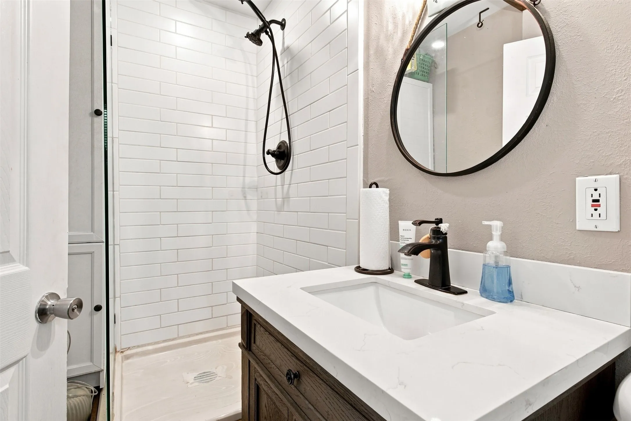 Subway tile shower surround with a dark bronze showerhead, a single vanity with a white countertop, and a dark bronze faucet