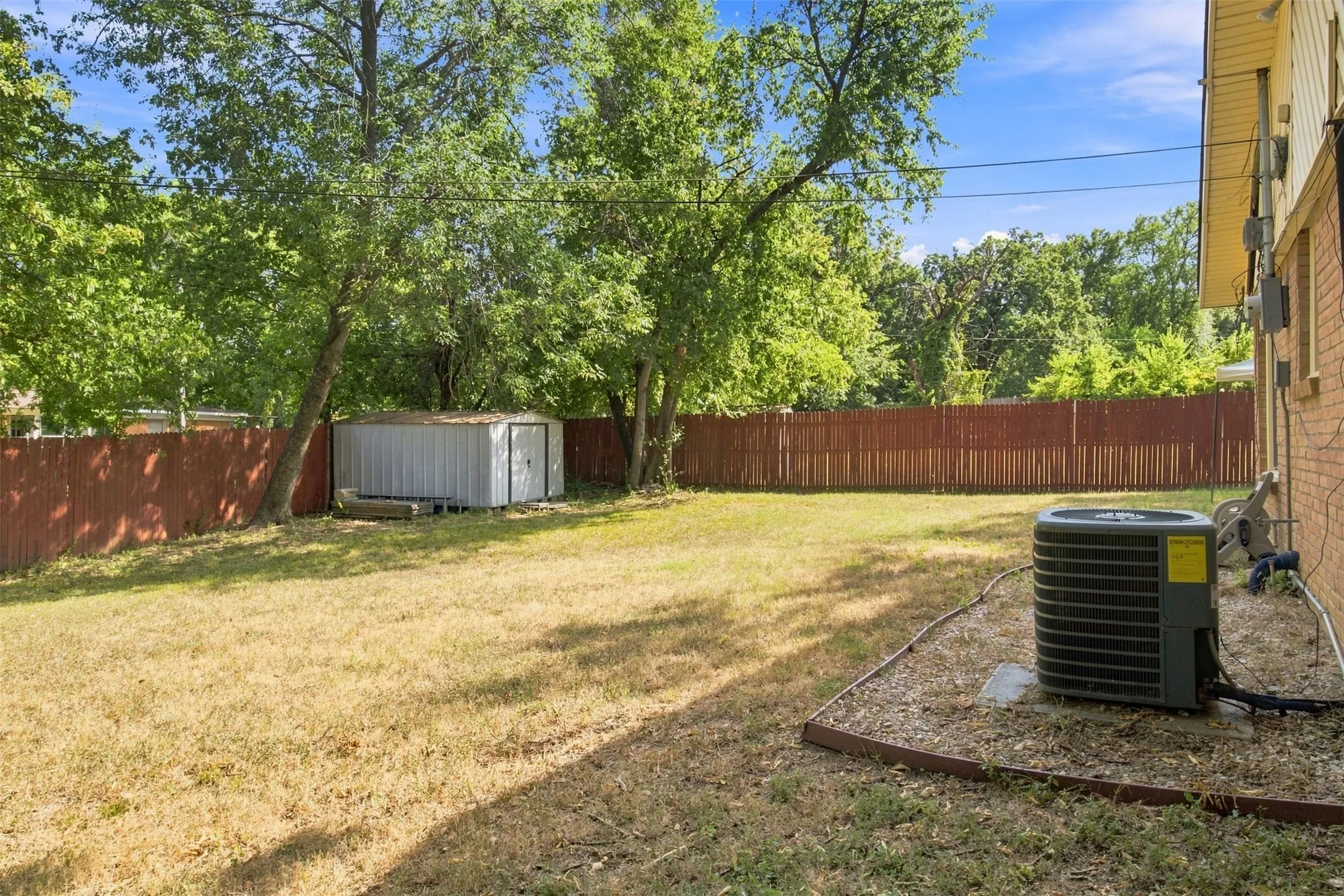 Expansive fenced backyard featuring a storage shed and mature trees