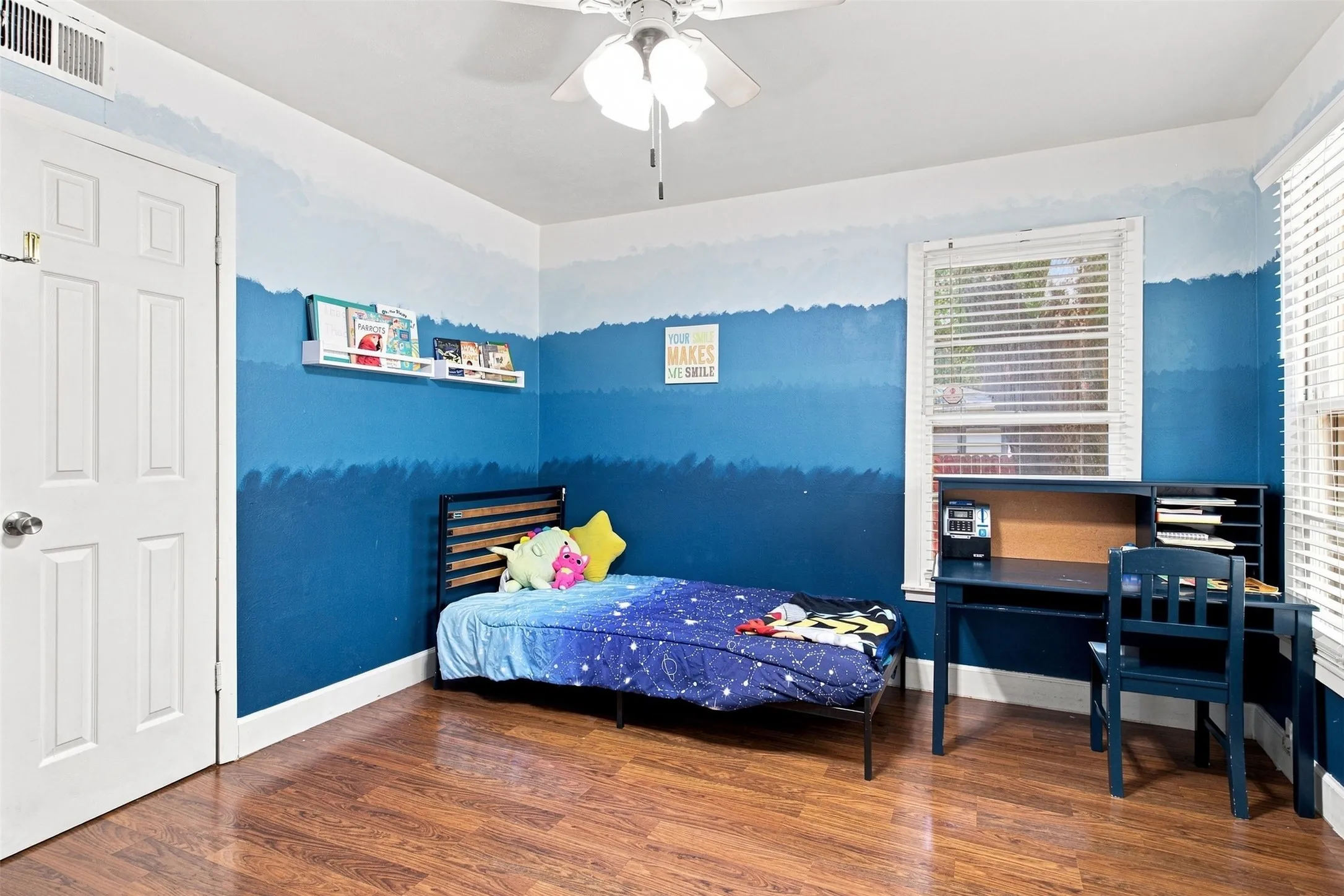 Wood-finish flooring, white paneled door, ceiling fan with light fixture, and window with blinds