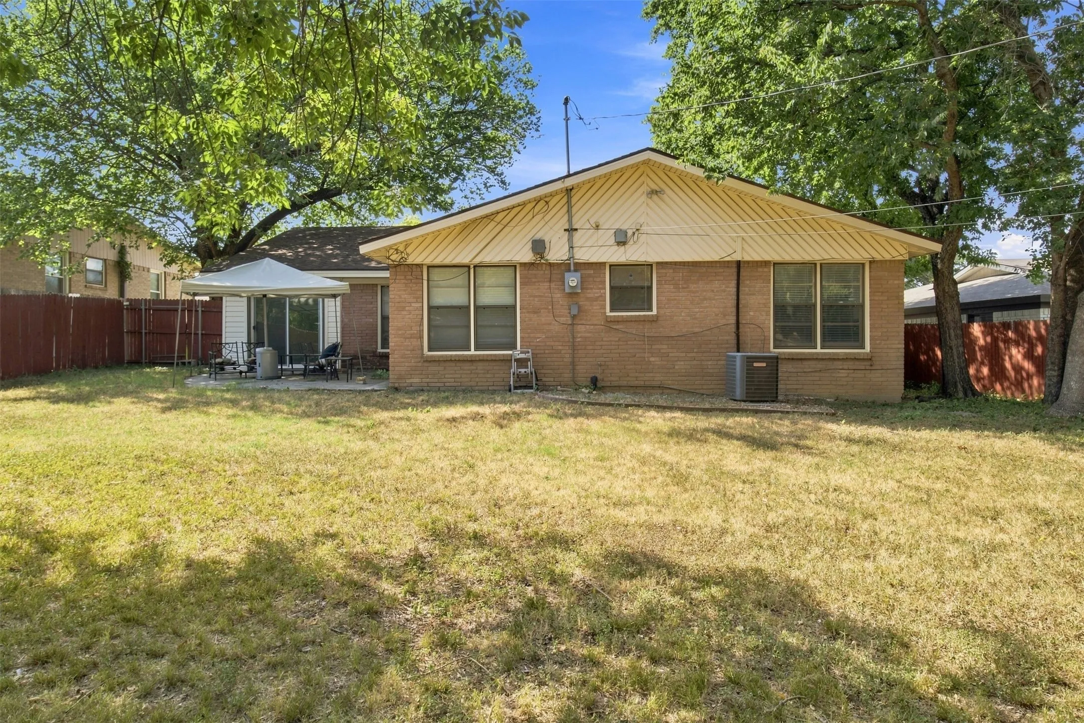 Rear exterior featuring brick siding, multiple windows, a concrete patio, and mature trees