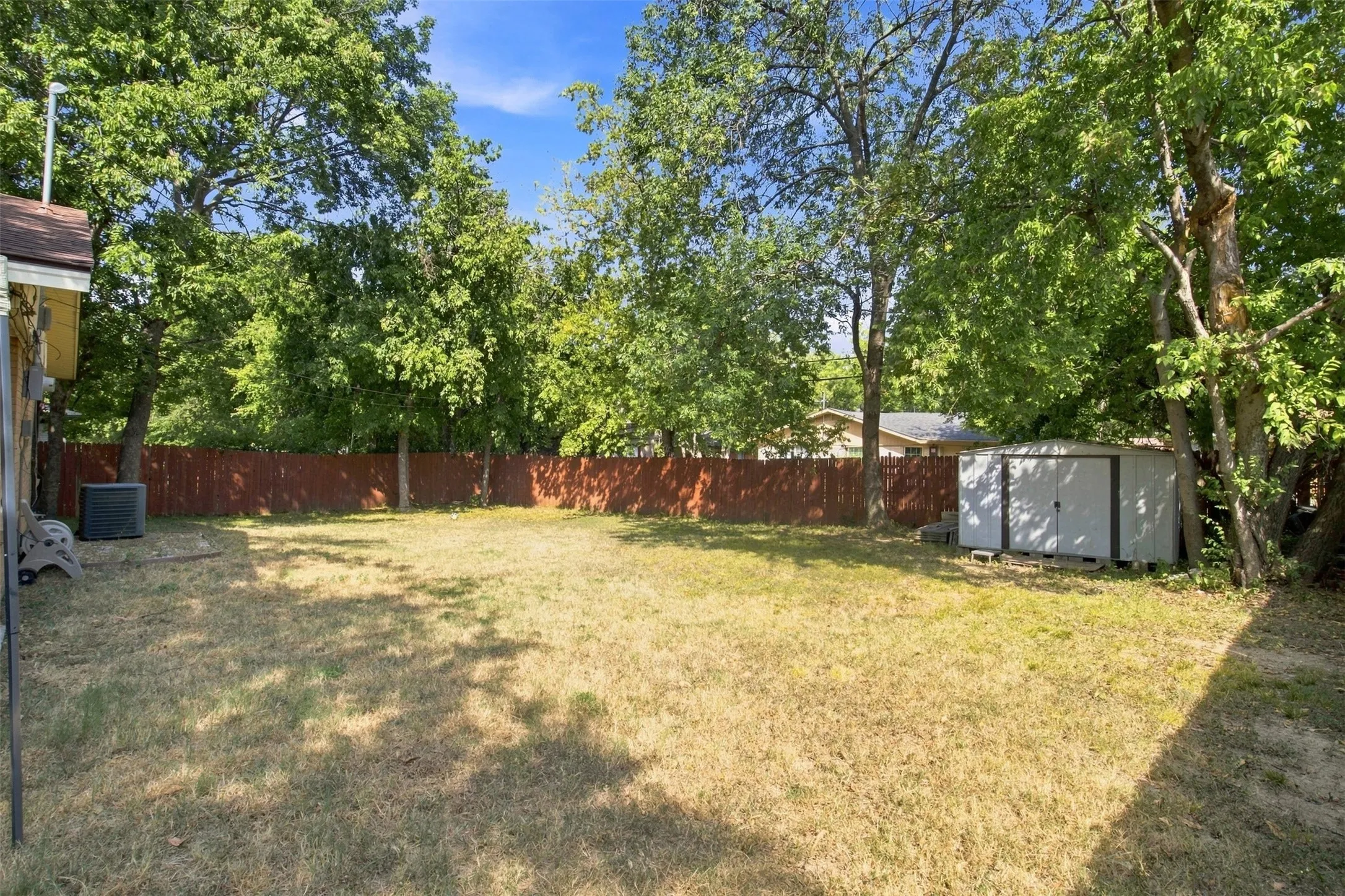 Expansive backyard featuring a privacy fence, mature trees, and a storage shed