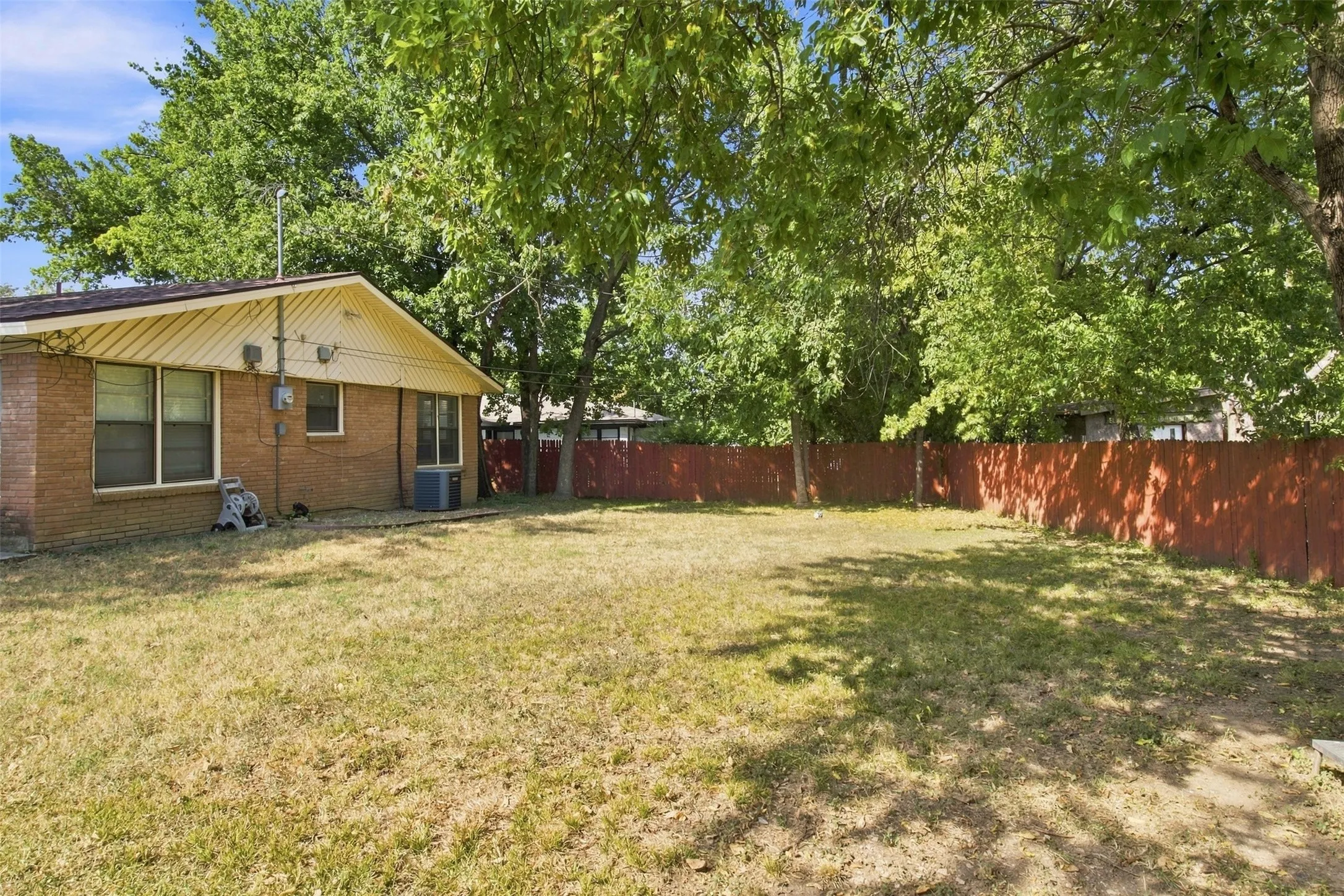 Expansive backyard featuring a red wood-panel fence and mature trees