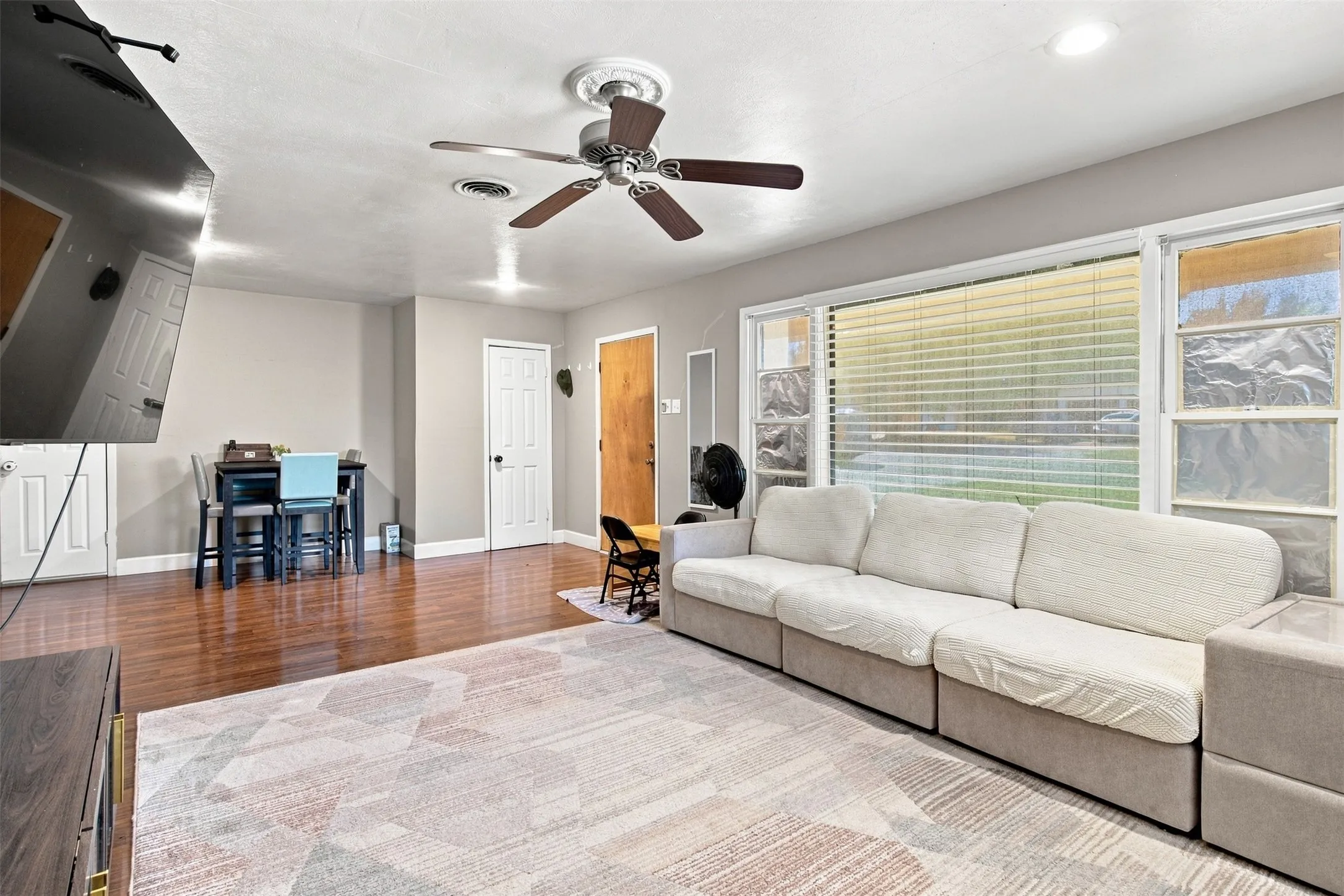 Spacious living area featuring wood-finish flooring, a ceiling fan, recessed lighting, and large windows