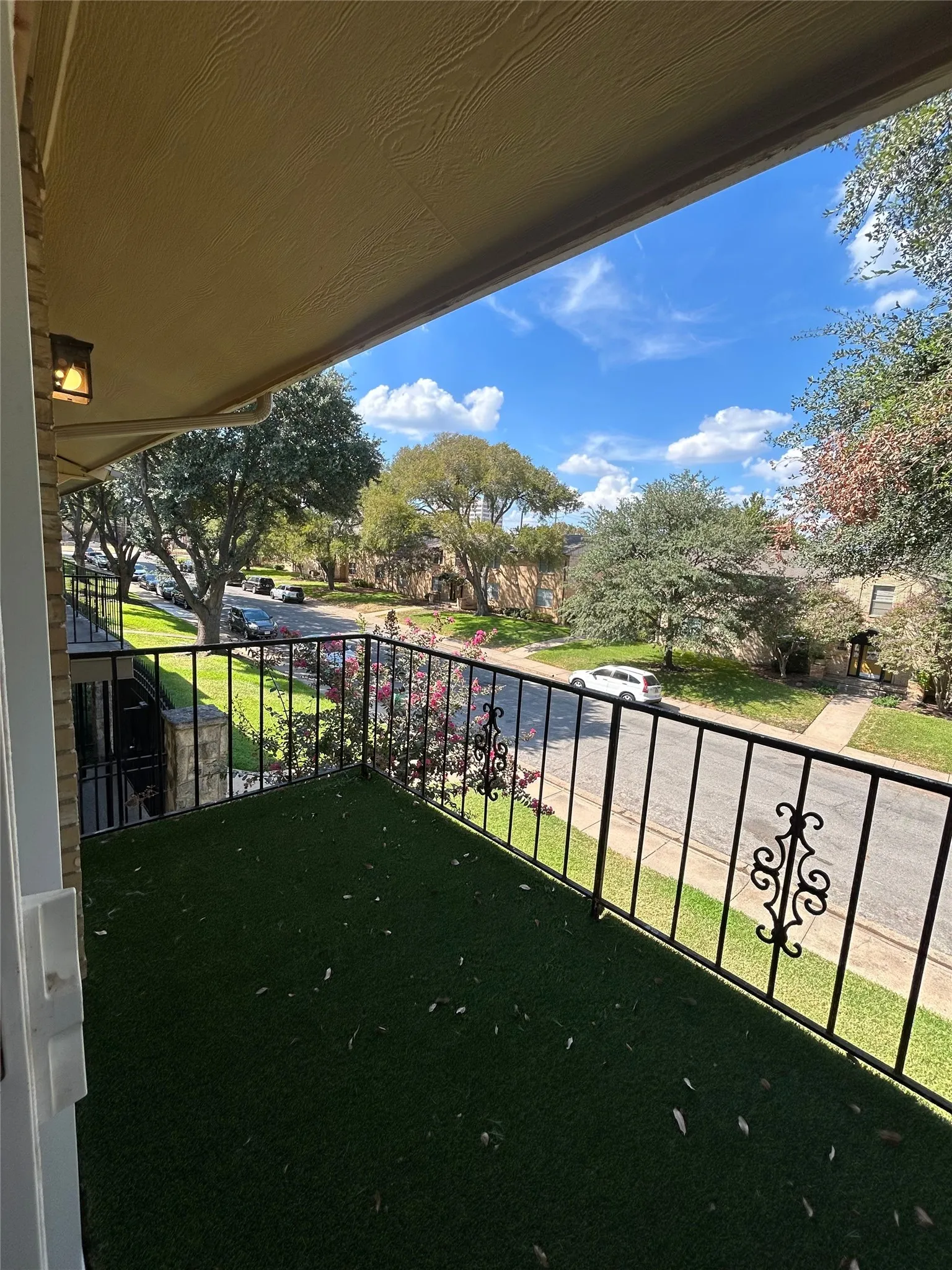 Balcony with decorative iron railing, artificial turf flooring, and an overhead light fixture