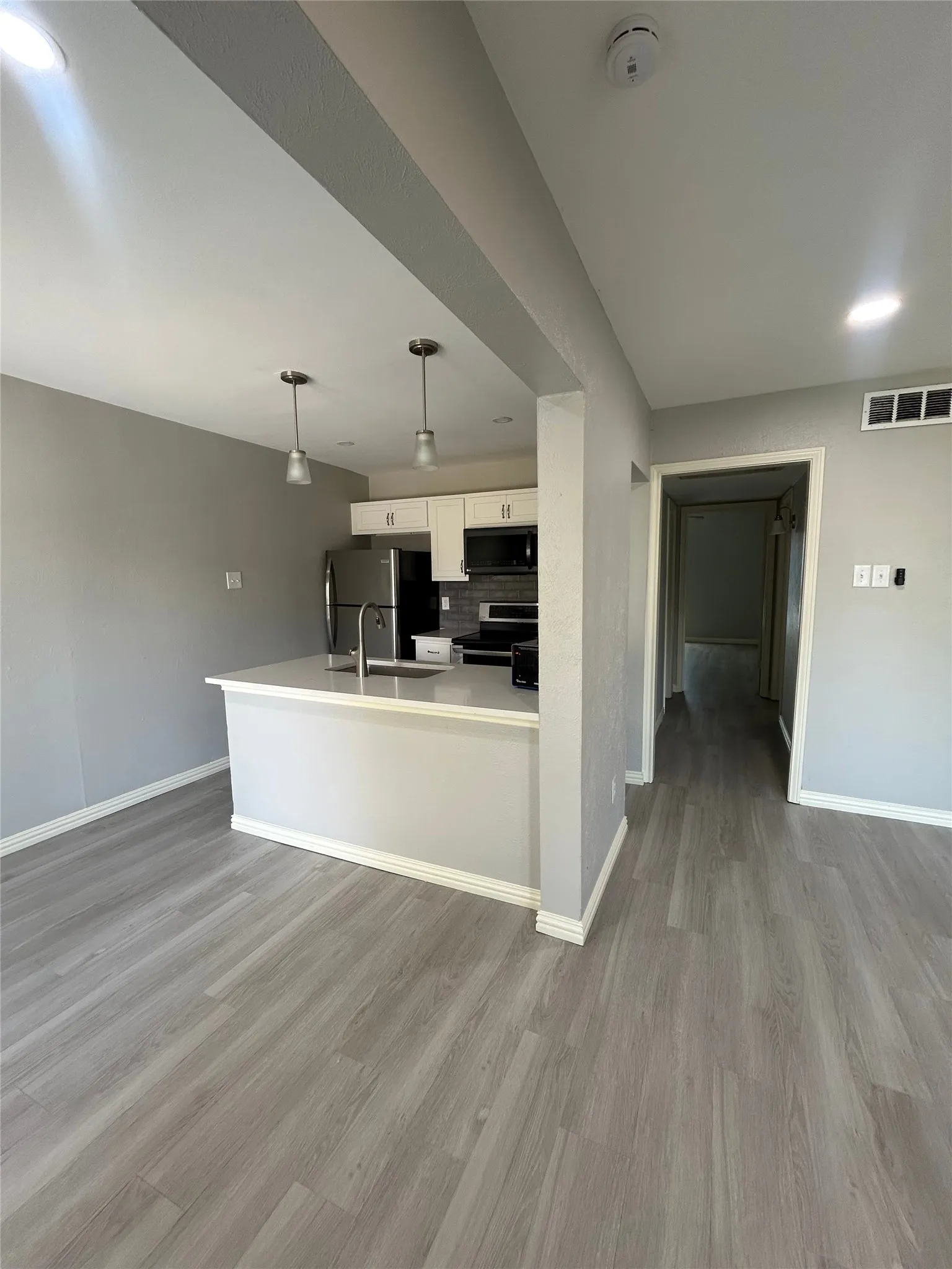 Open-concept living area featuring wood-finish flooring, recessed lighting, and a kitchen with white cabinetry, stainless steel appliances, and a breakfast bar