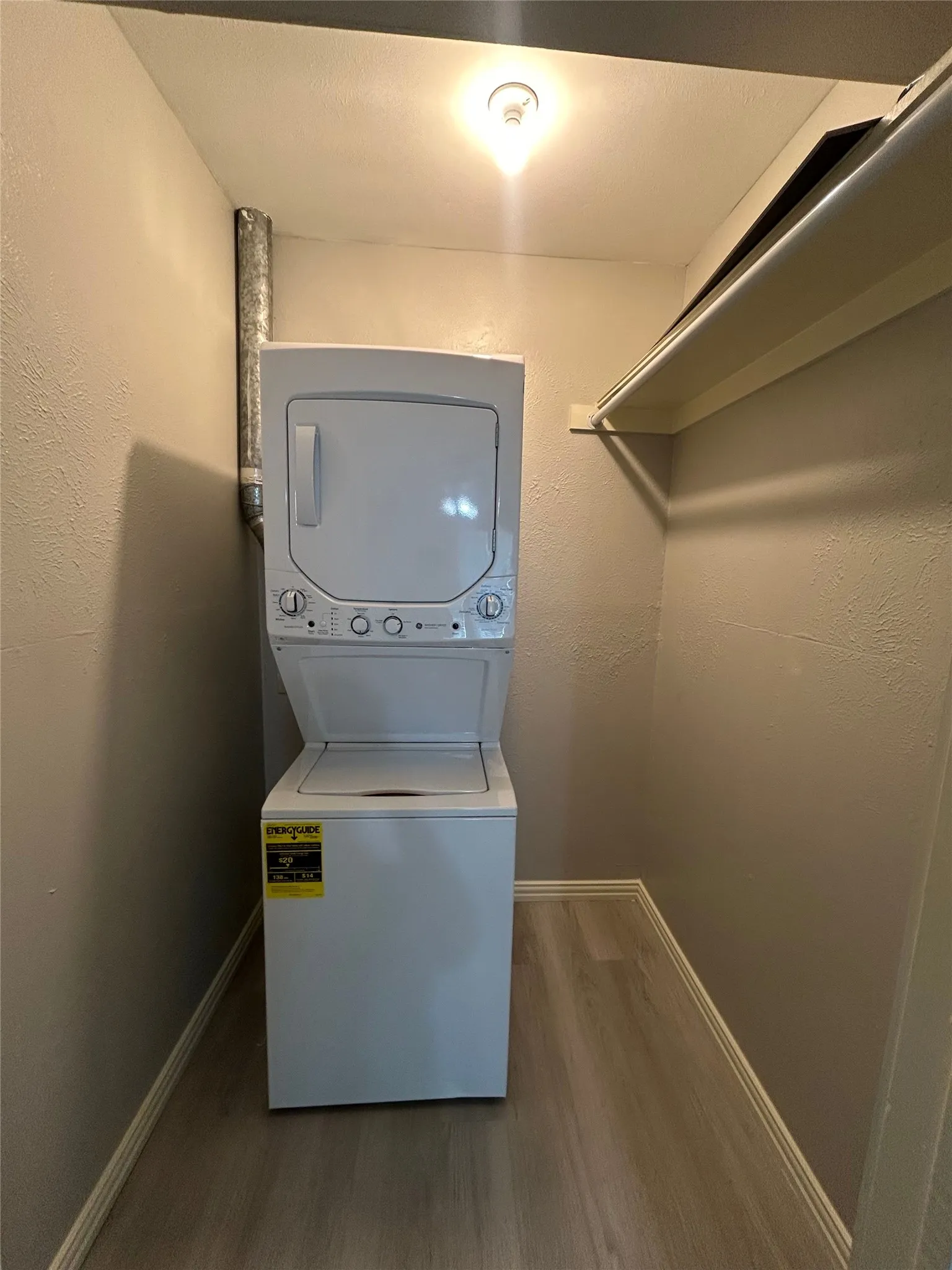 Dedicated laundry area featuring a stacked washer and dryer, wood-finish flooring, and overhead shelving
