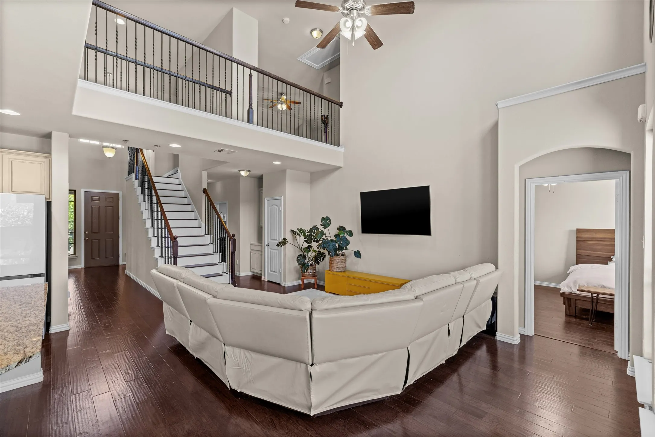 Two-story living area with high ceilings, wood-finish flooring, a wrought-iron staircase, a second-story landing with matching railing, and recessed lighting