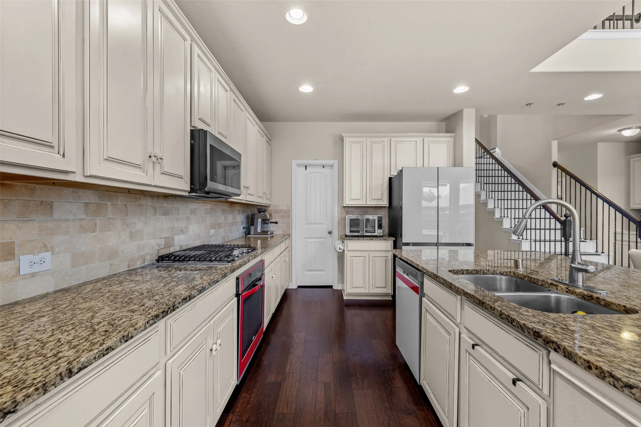 Kitchen featuring wood-finish flooring, stone countertops, white cabinetry, a gas range, and a dual basin sink