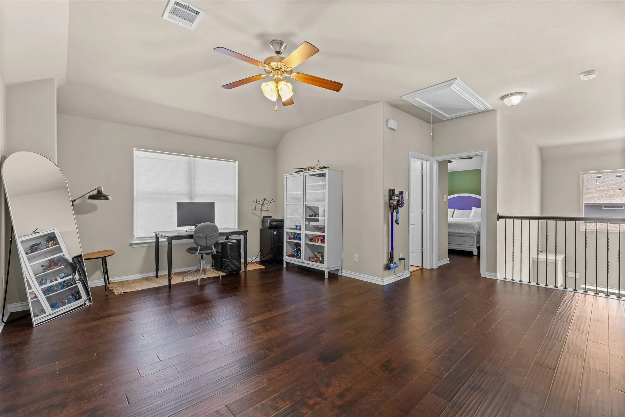 Spacious open area featuring dark wood-finish flooring, a window with blinds, an overhead ceiling fan, and a metal spindle railing