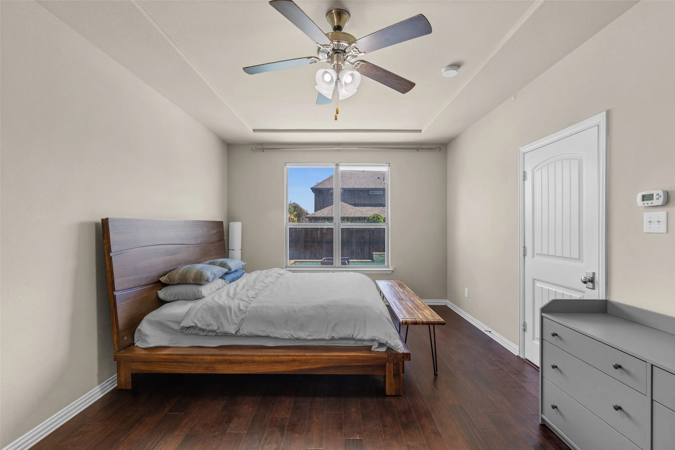 Tray ceiling with a ceiling fan, wood-finish flooring, and a single window