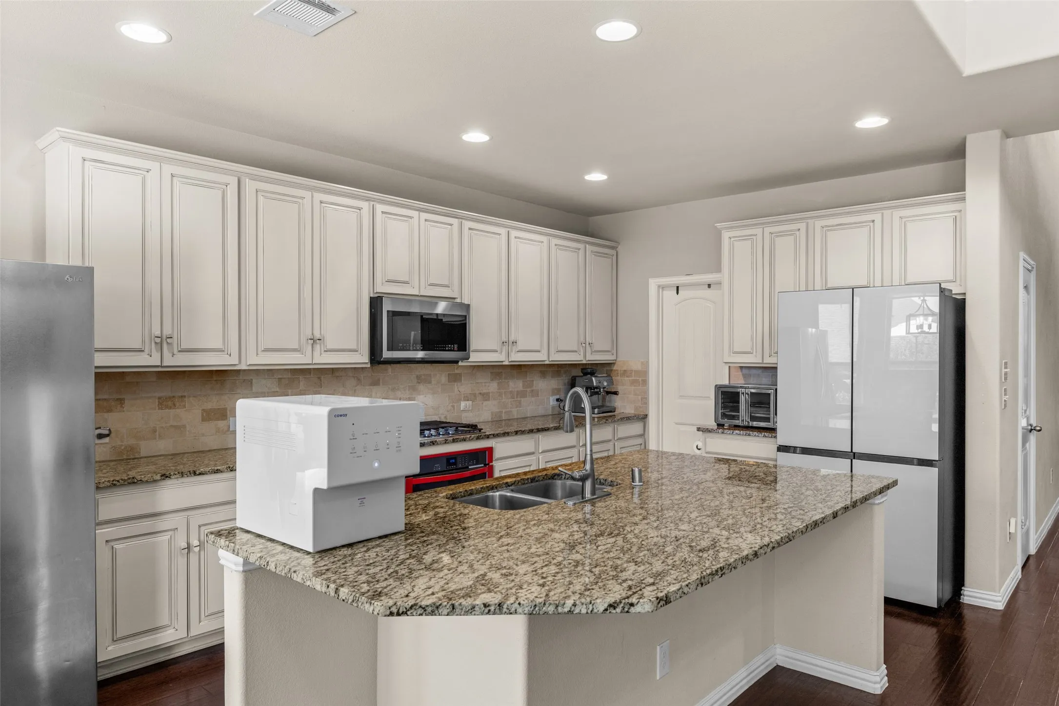 Kitchen featuring extensive light-toned cabinetry, a large kitchen island with a double basin sink, stainless steel appliances, and wood-finish flooring