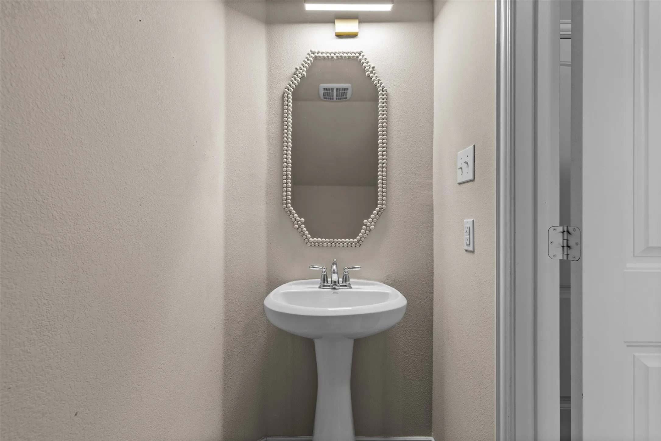 Pedestal sink with chrome faucet, illuminated by an overhead light fixture