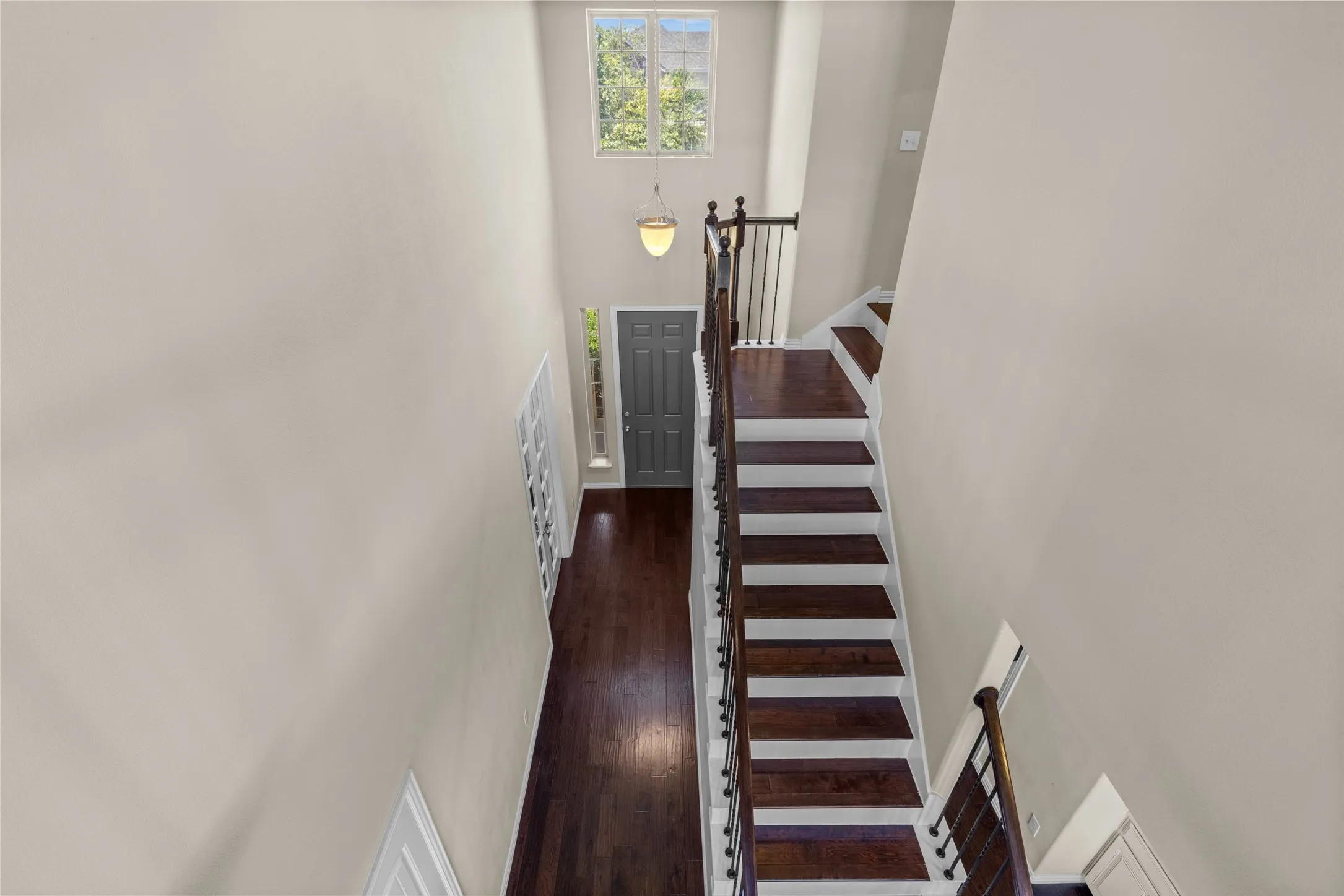 Two-story entryway with dark wood-finish flooring, a contemporary pendant light fixture, and a staircase featuring wood treads and a black metal railing