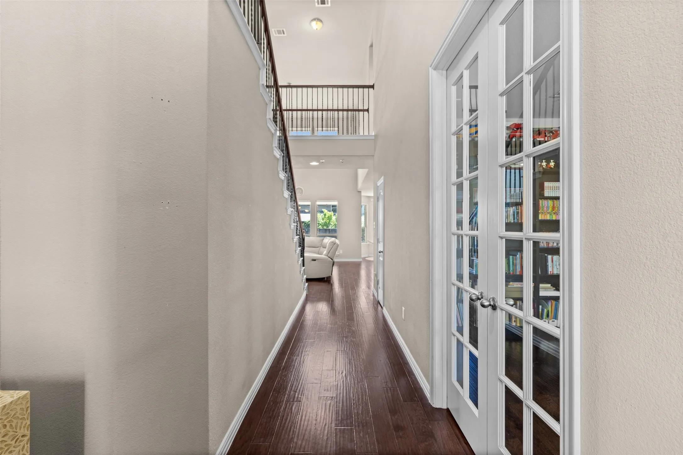Hardwood flooring, white paneled French doors, white trim, and a staircase with a dark wood handrail and black balusters