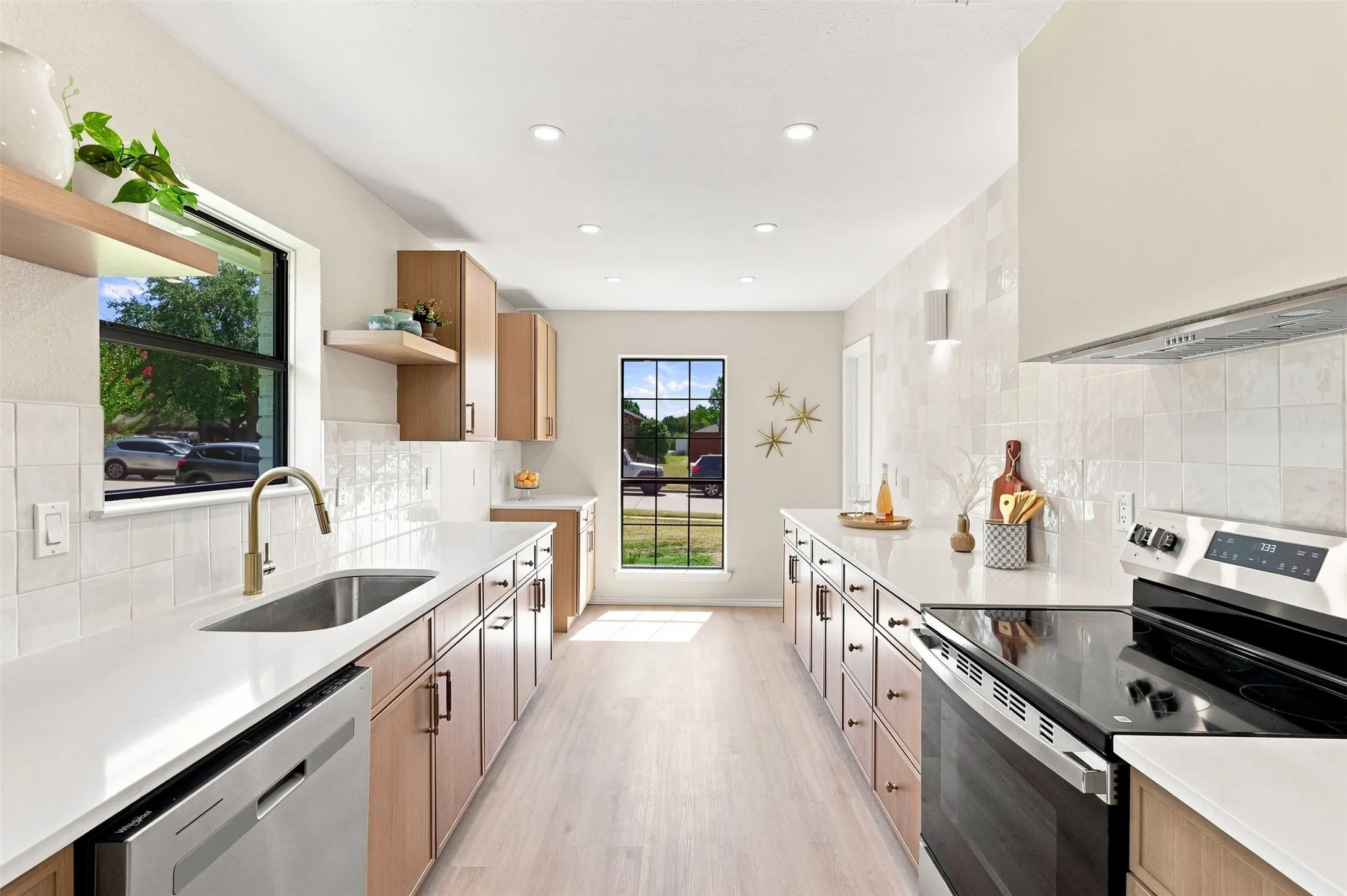 Galley kitchen featuring light wood-finish cabinetry, light countertops, integrated sink with a gooseneck faucet, stainless steel appliances, and wood-finish flooring