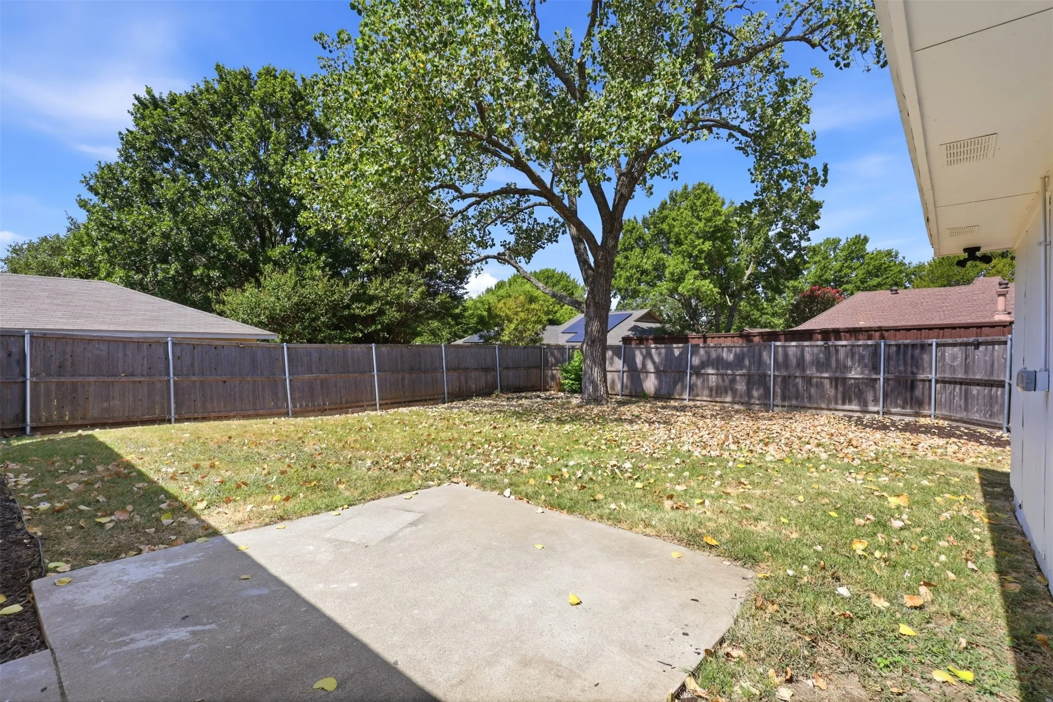 Spacious backyard with a large concrete patio, mature tree, and wood privacy fencing