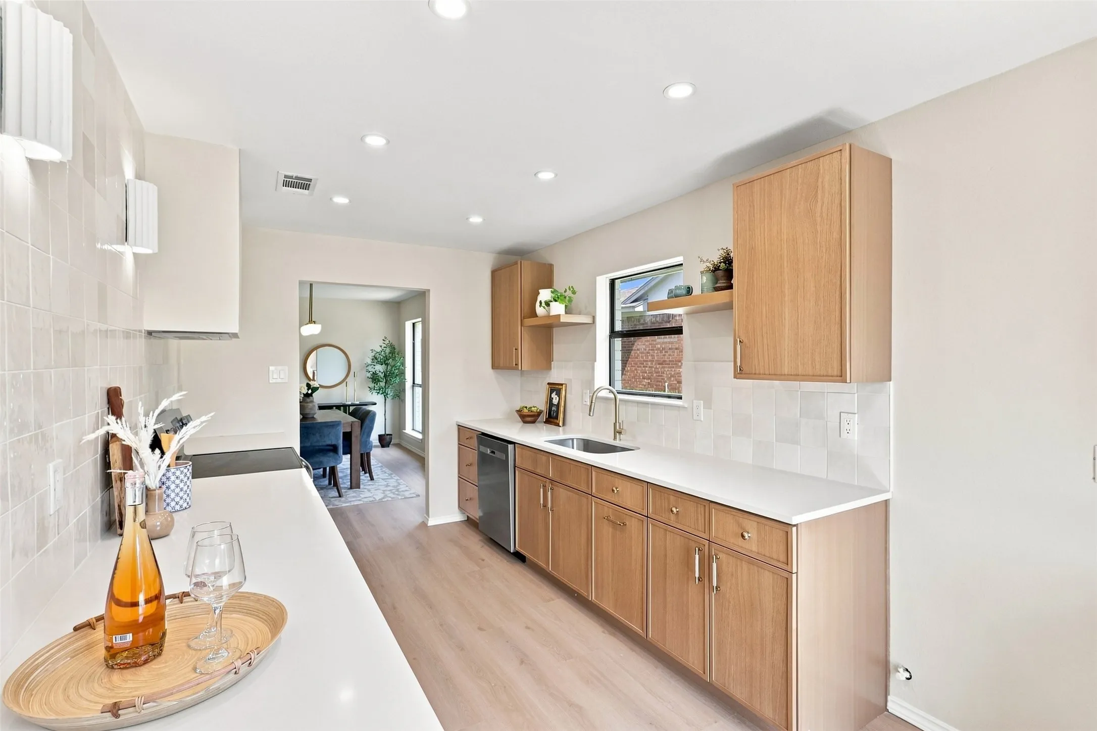 Wood-finish cabinetry, light-toned countertops, tile backsplash, built-in stainless steel dishwasher, and recessed lighting