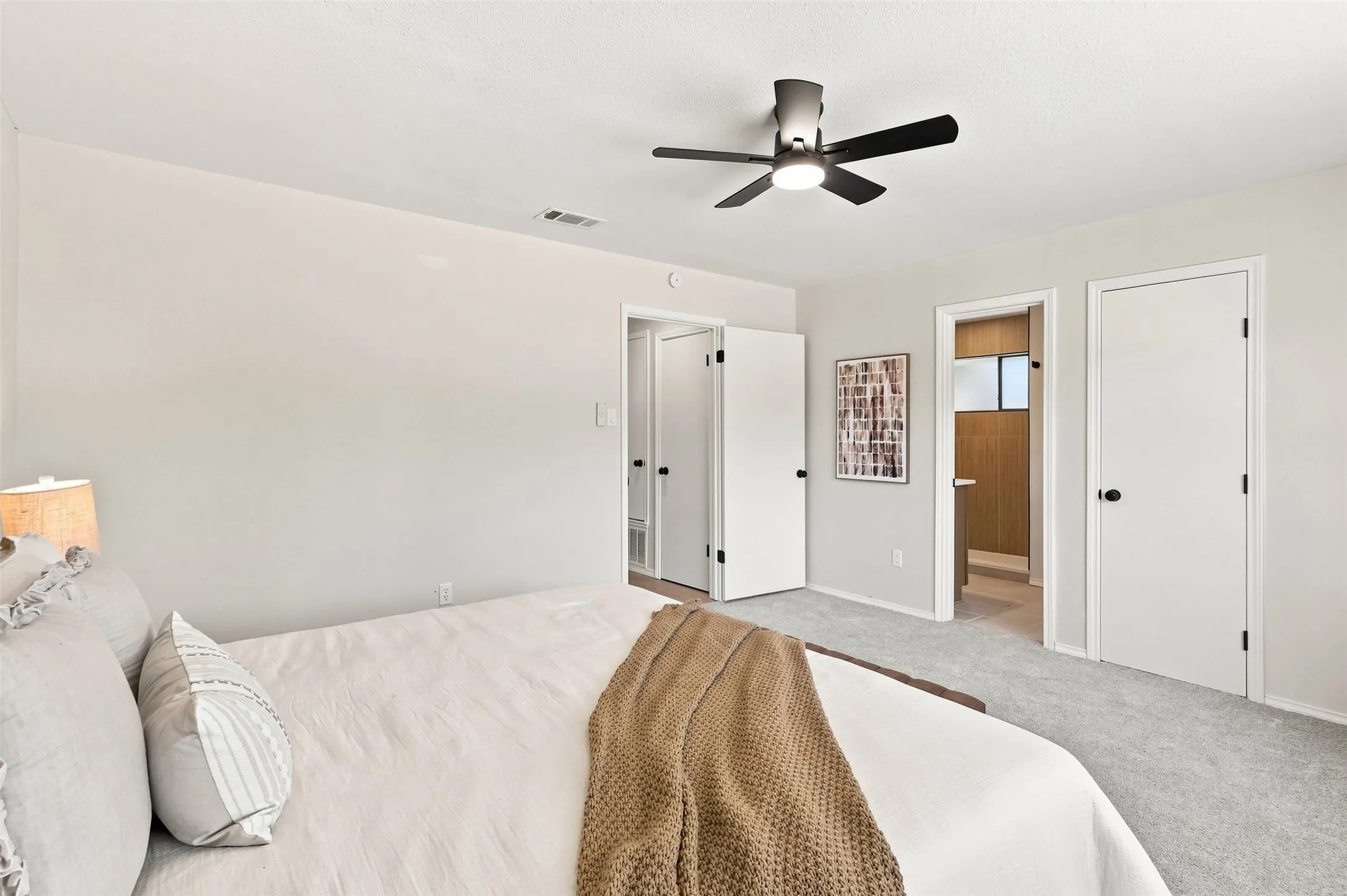 Carpeted flooring, light-toned walls, ceiling fan, and multiple white doors with black hardware