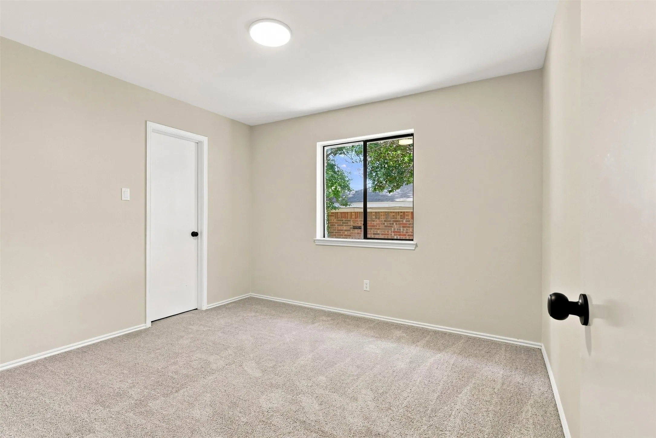 Neutral tone wall paint, light gray carpeting, white trim, recessed lighting, and a window with a brick exterior visible
