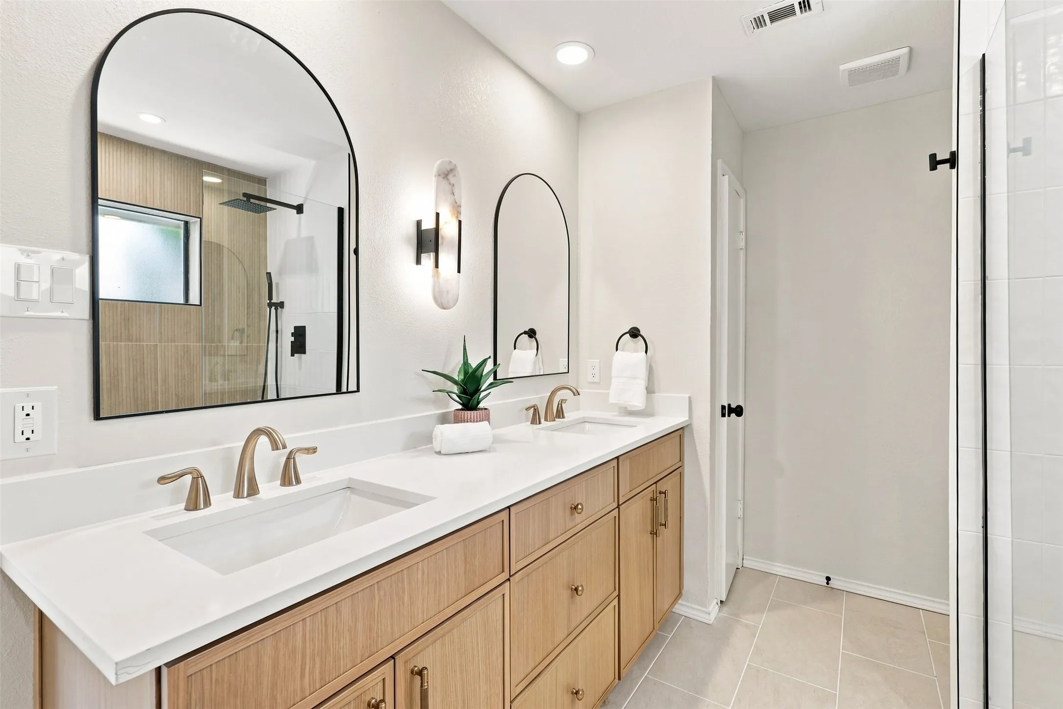 Dual arched mirrors, dual undermount sinks, wood-finish cabinetry, quartz countertops, and a glass-enclosed shower
