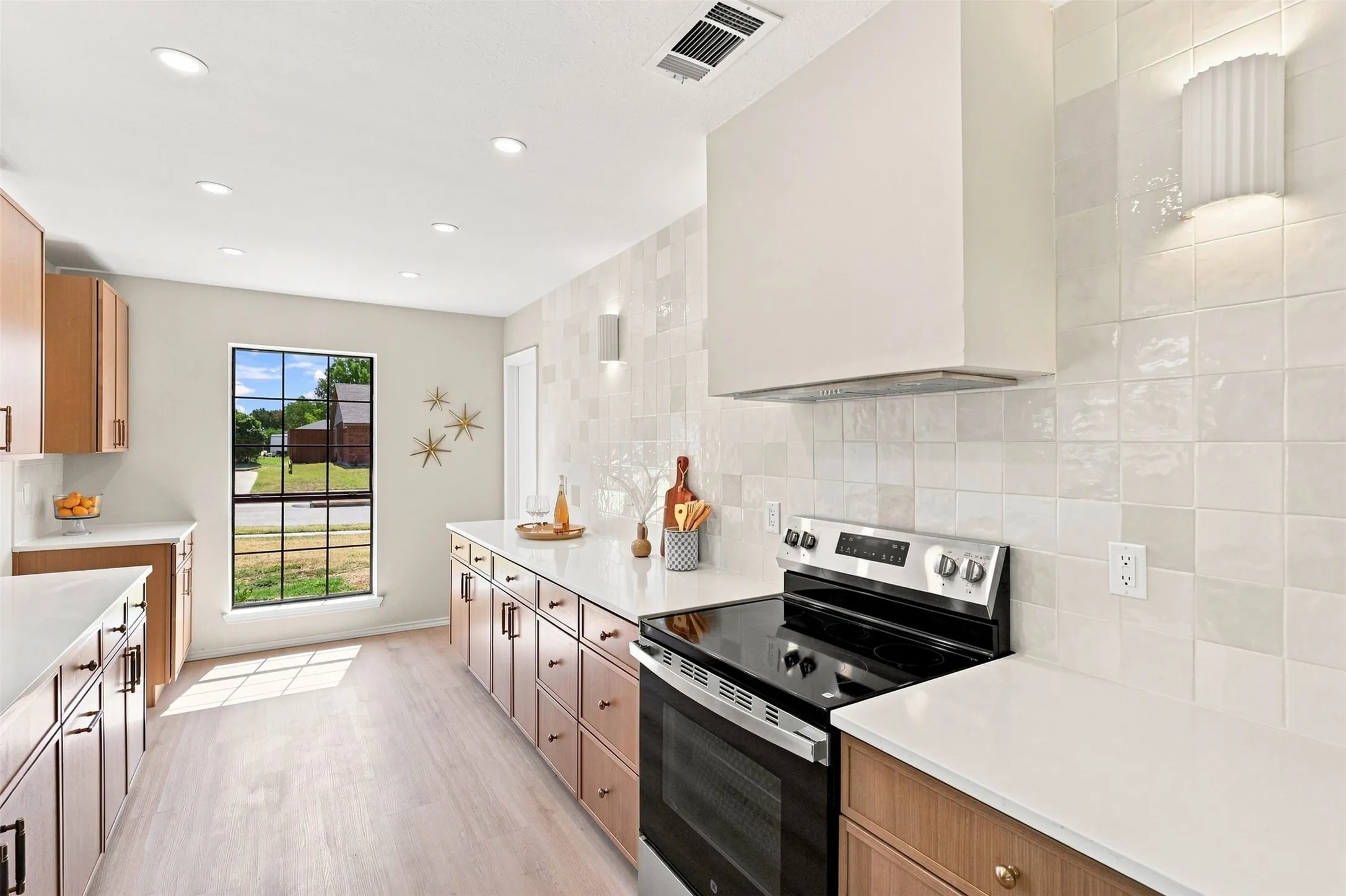 Recessed lighting, wood-finish cabinetry with black hardware, white countertops, tile backsplash, and a black range