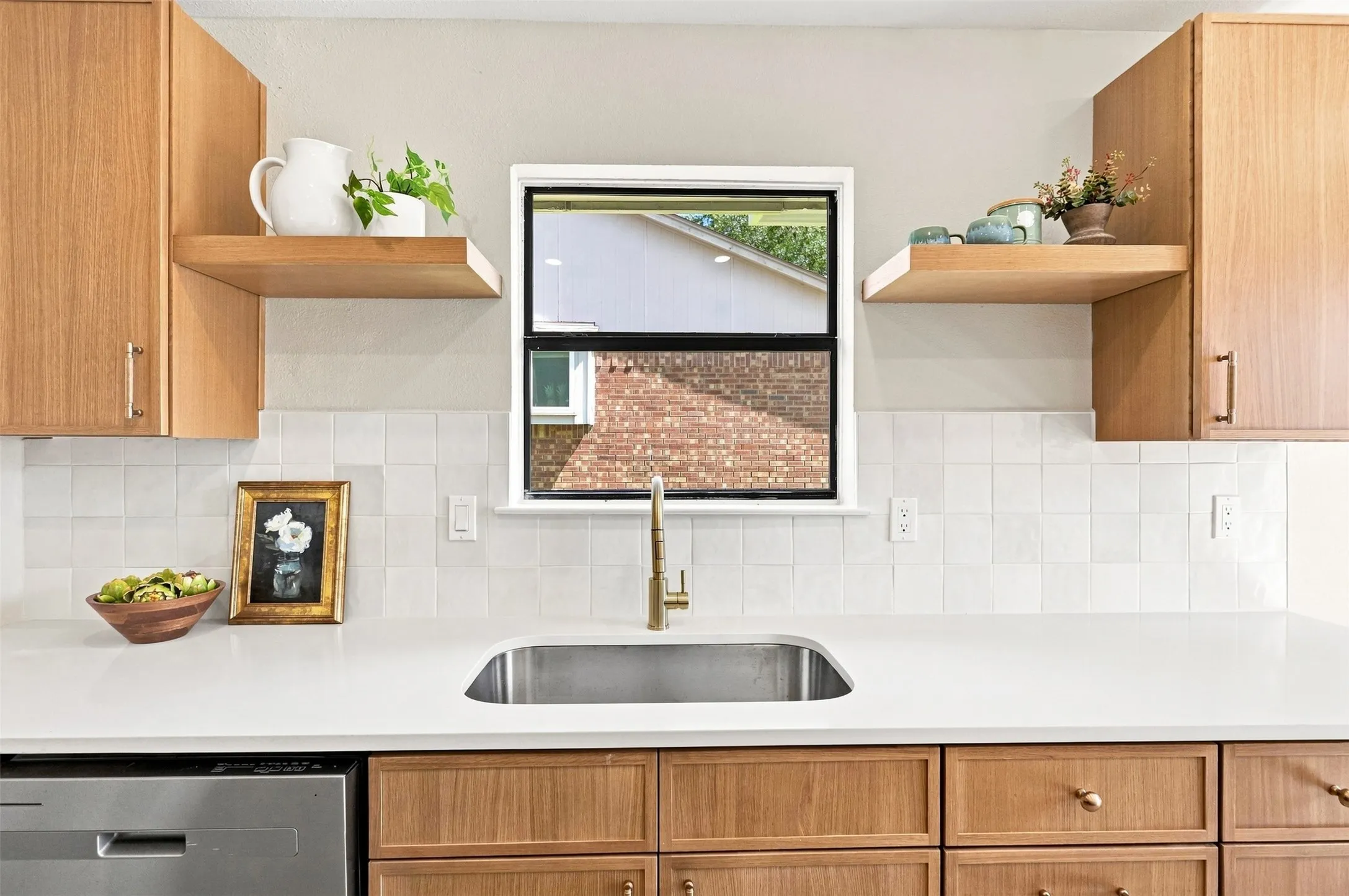 Stainless steel sink with a gold-tone faucet, white countertops, square tile backsplash, and light wood-finish cabinetry