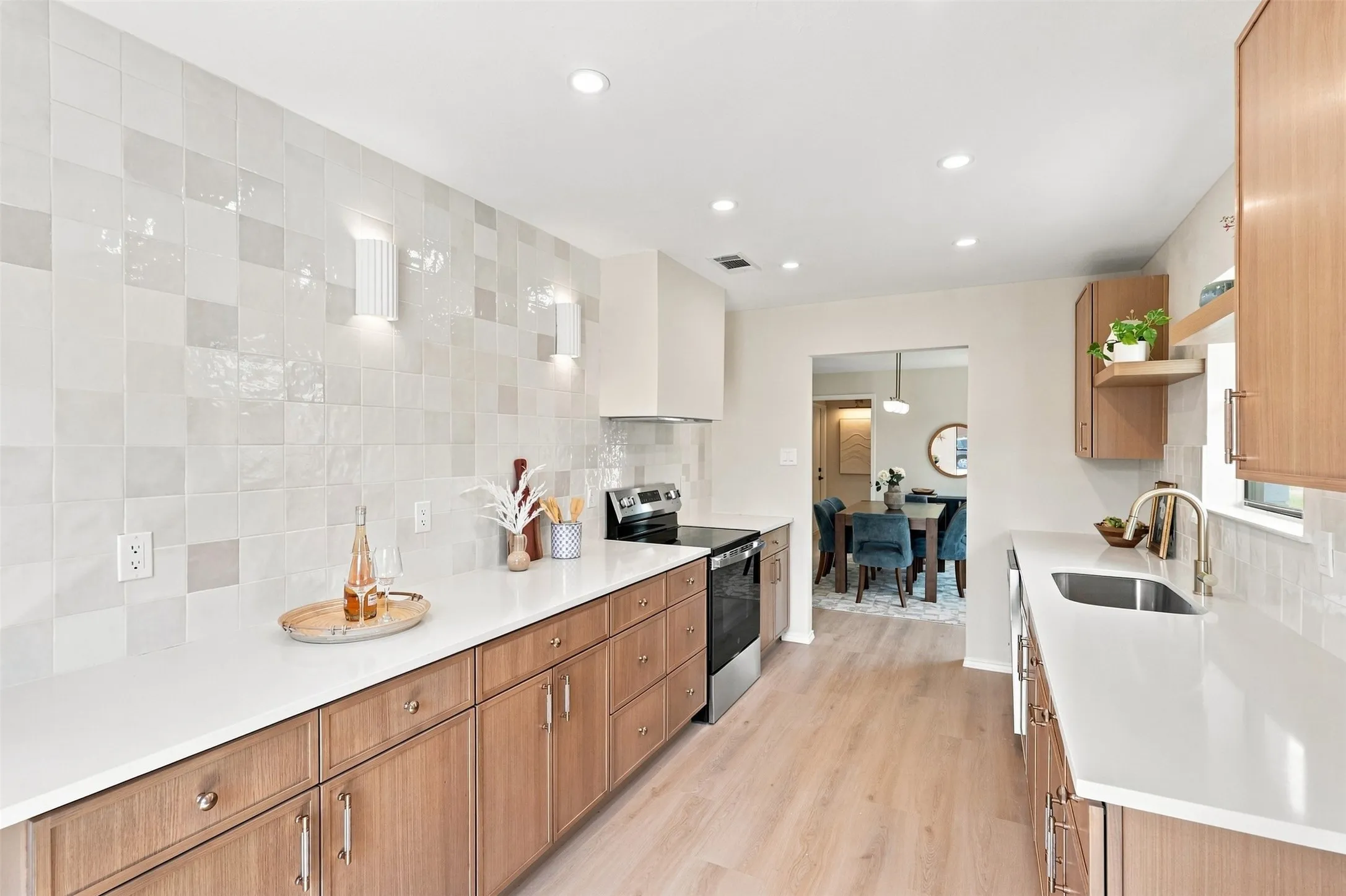 Modern kitchen featuring wood-finish cabinetry, light countertops, integrated stainless steel appliances, and recessed lighting