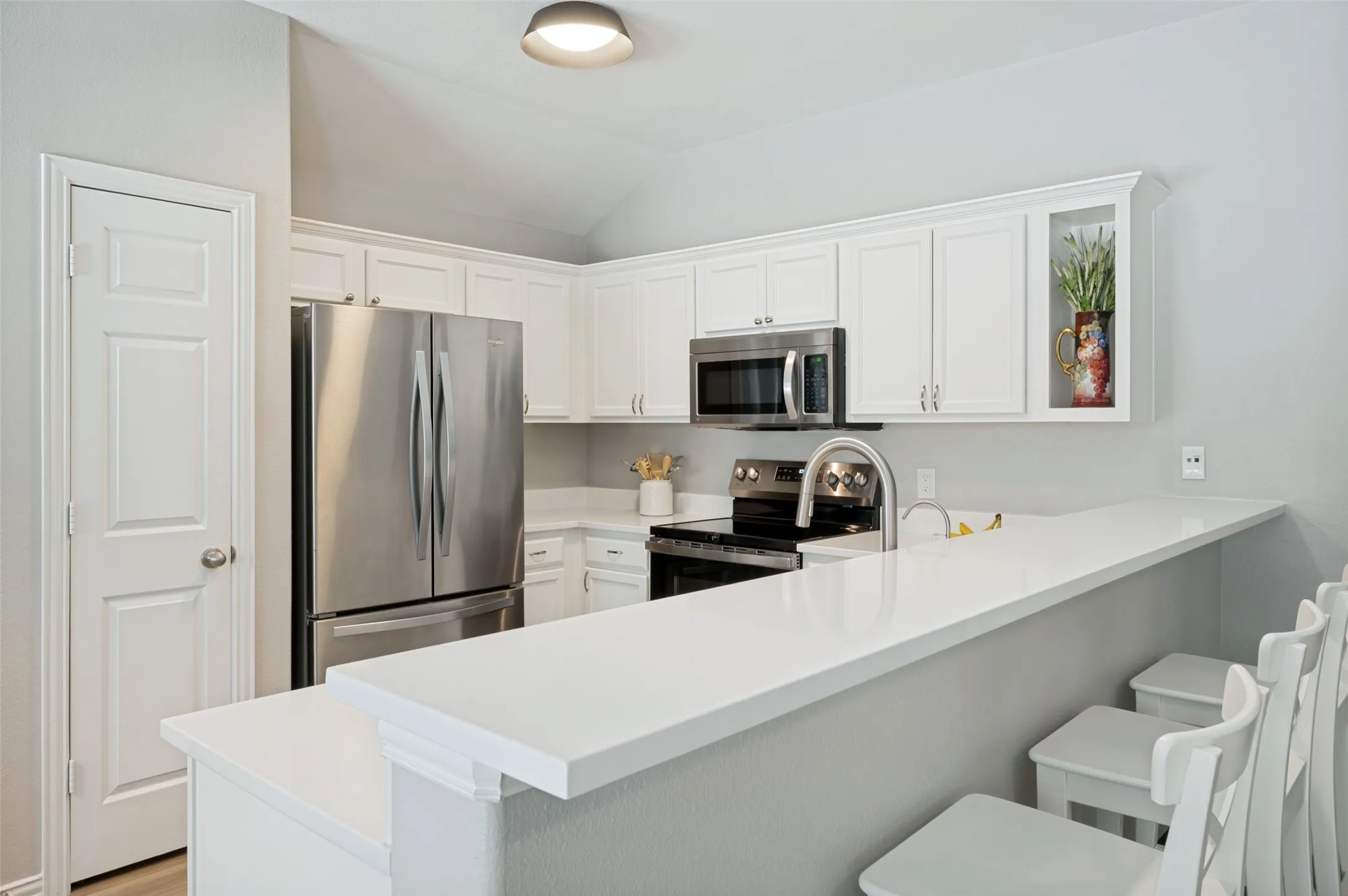 White shaker cabinetry, stainless steel appliances, white countertops, built-in microwave, and a breakfast bar