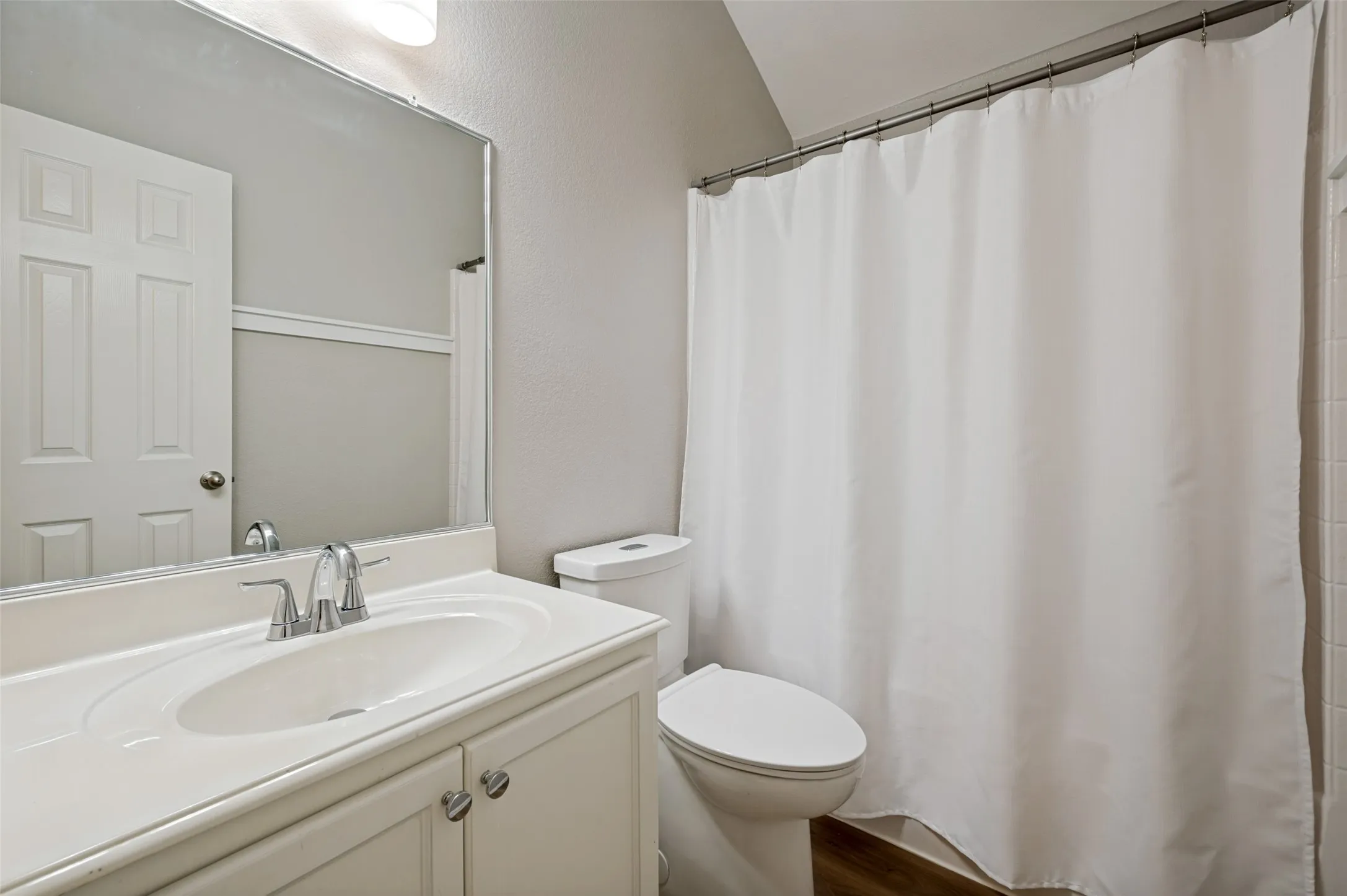 Vanity with an integrated sink and chrome faucet, white paneled door, and a toilet