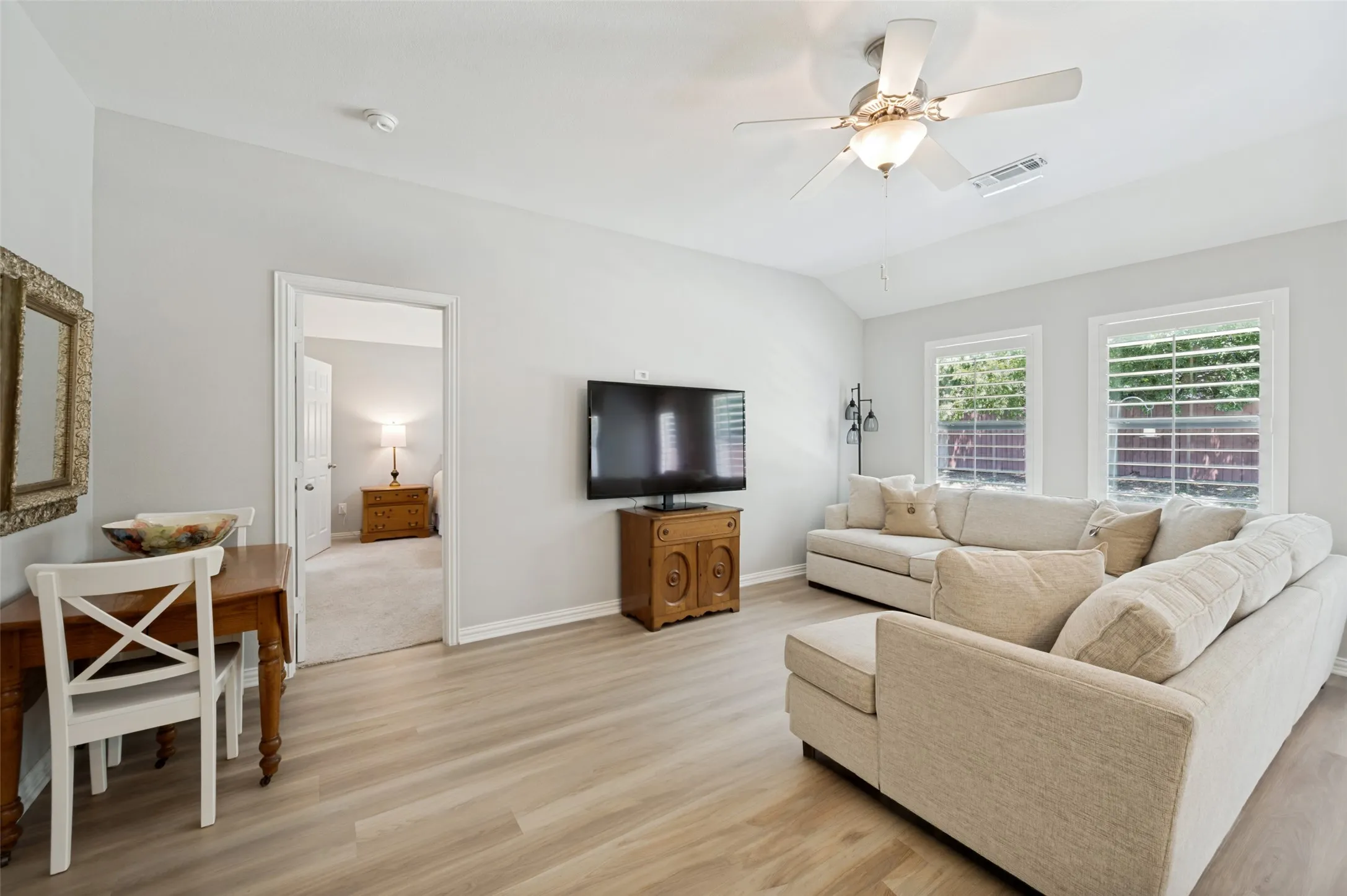 Vaulted ceilings, wood-finish flooring, ceiling fan, and two windows with plantation shutters