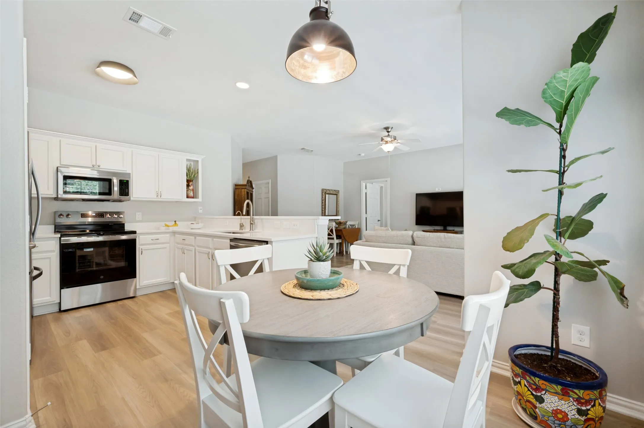Kitchen featuring white cabinetry, stainless steel appliances, solid surface countertops, wood-finish flooring, and a breakfast bar